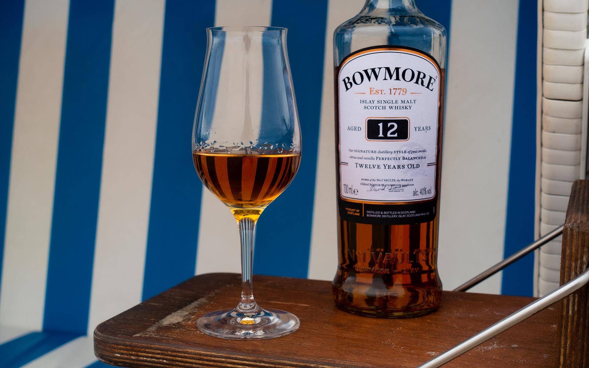 木托盤上的Bowmore威士忌酒瓶和玻璃杯，條紋背景。