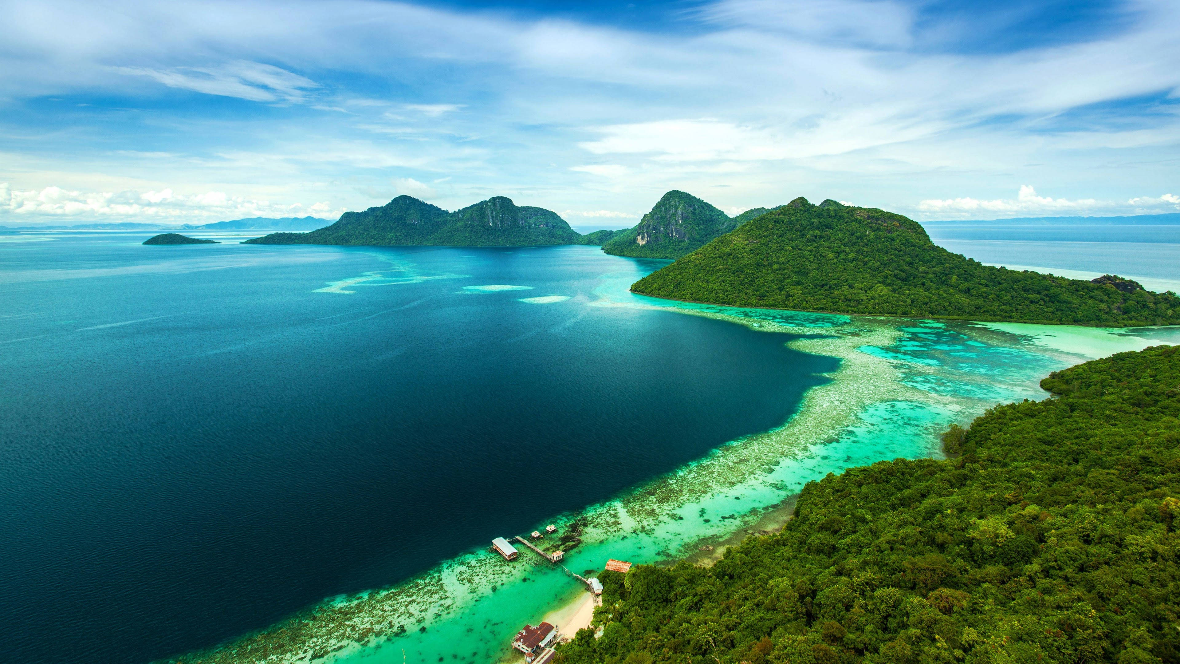 波海迪蘭島 壁紙 — 從空中俯瞰鬱鬱蔥蔥的綠色島嶼，周圍環繞著充滿活力的碧綠海水和深藍色海洋，天空部分多雲。
