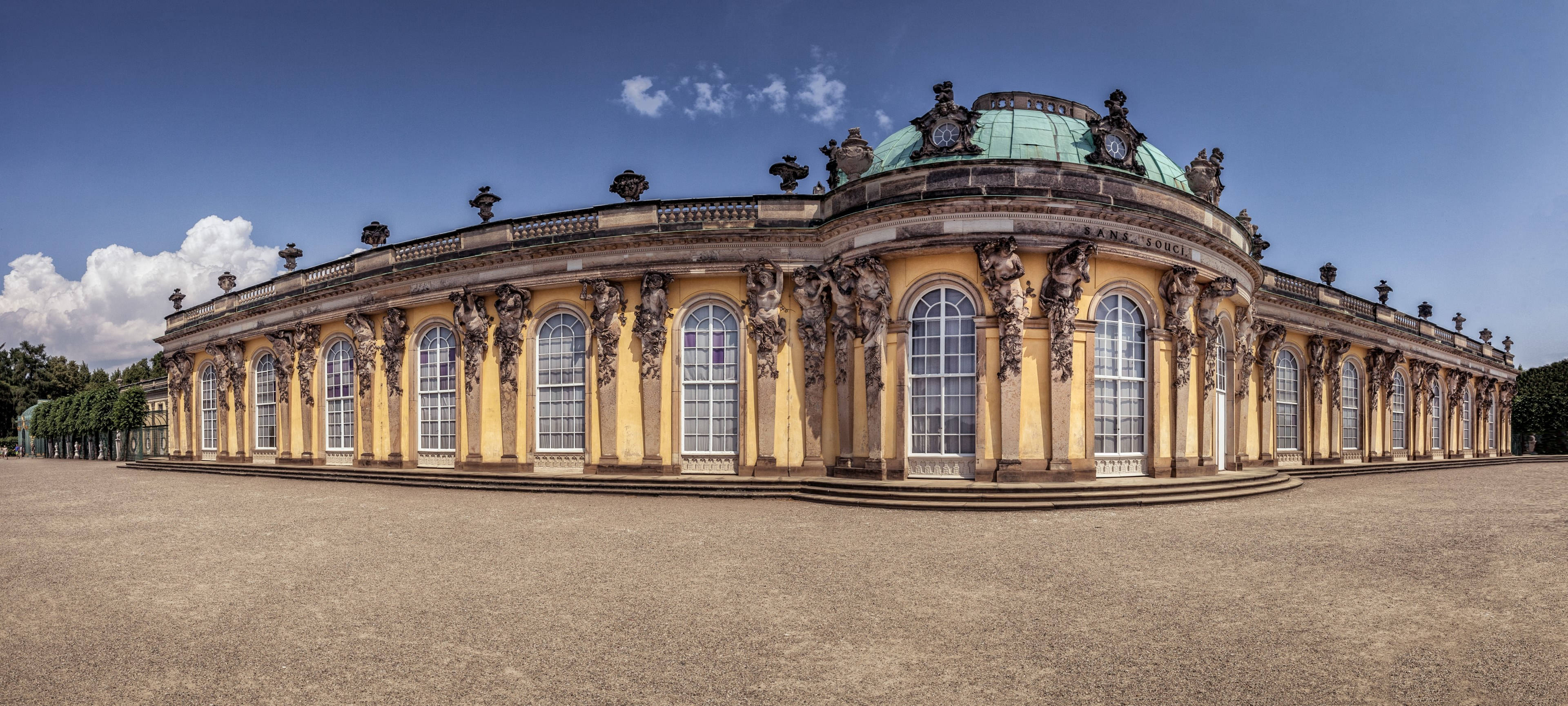 波茨坦桑蘇西宮殿全景 壁紙 — 一座宏偉的弧形巴洛克宮殿，飾有華麗的雕塑和綠色圓頂，在明亮的藍天和蓬鬆的白雲下。