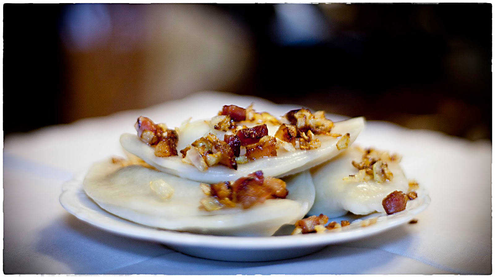波蘭波奇基（Pierogi Ruskie） 壁紙 — 白碟上蒸餃子配脆煙肉和堅果的特寫。