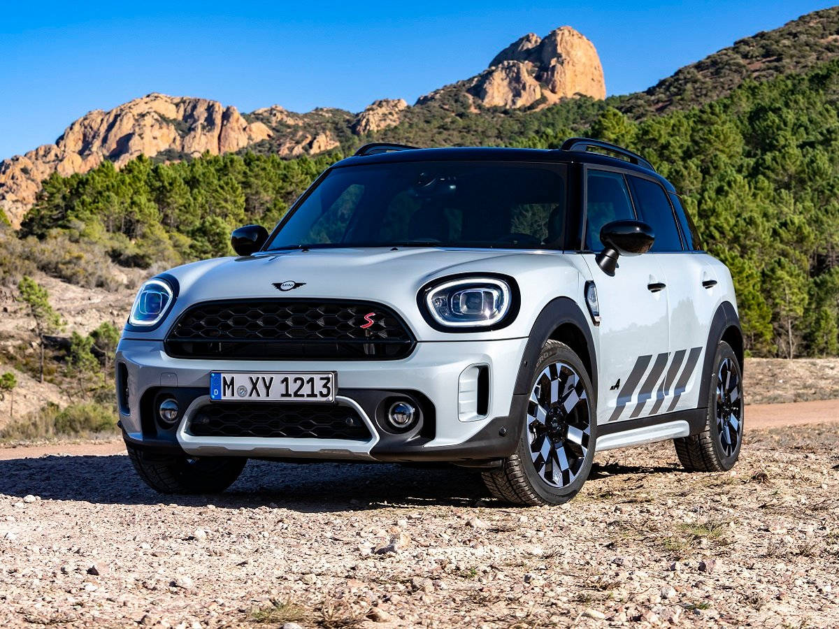 泥地上停泊的灰黑迷你車 壁紙 — 一輛銀色MINI Countryman S大膽地停在陽光明媚的碎石路上，背景是崎嶇的山脈和綠樹。
