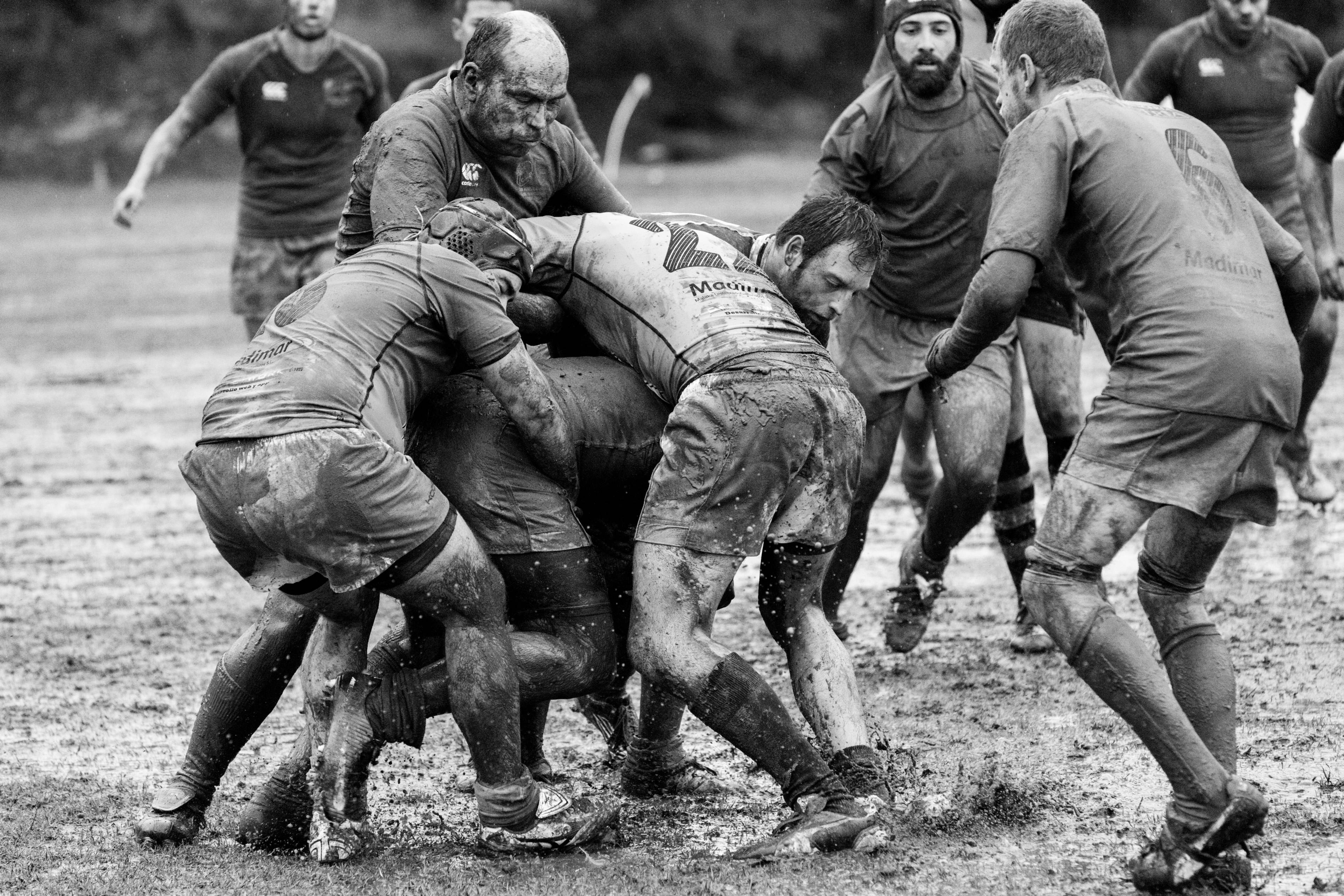 泥濘 rugby 搏鬥攝影 壁紙 — 黑白照片，草地上欖球球員在泥濘的爭球中糾纏。