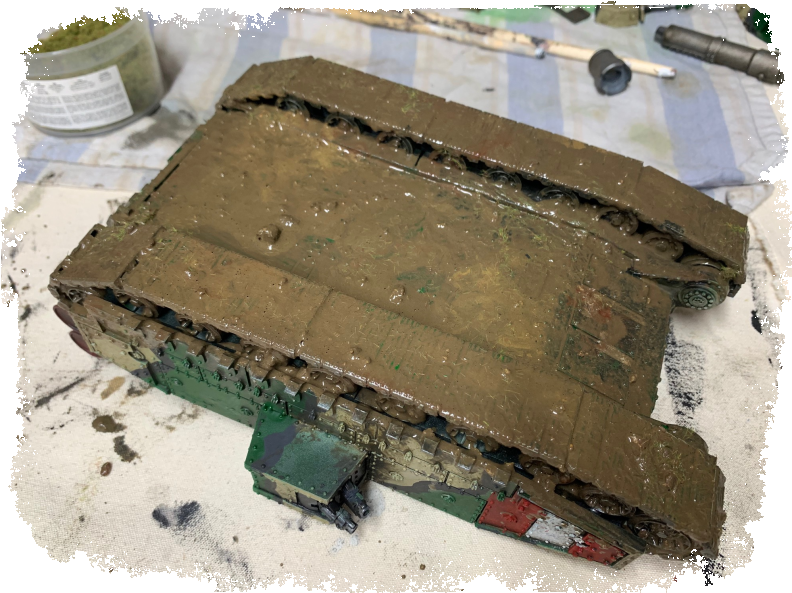 泥濘軍用坦克模型 壁紙 — 一個風化的軍用坦克模型放在濺滿油漆的工作枱上，周圍是模型工具和油漆。