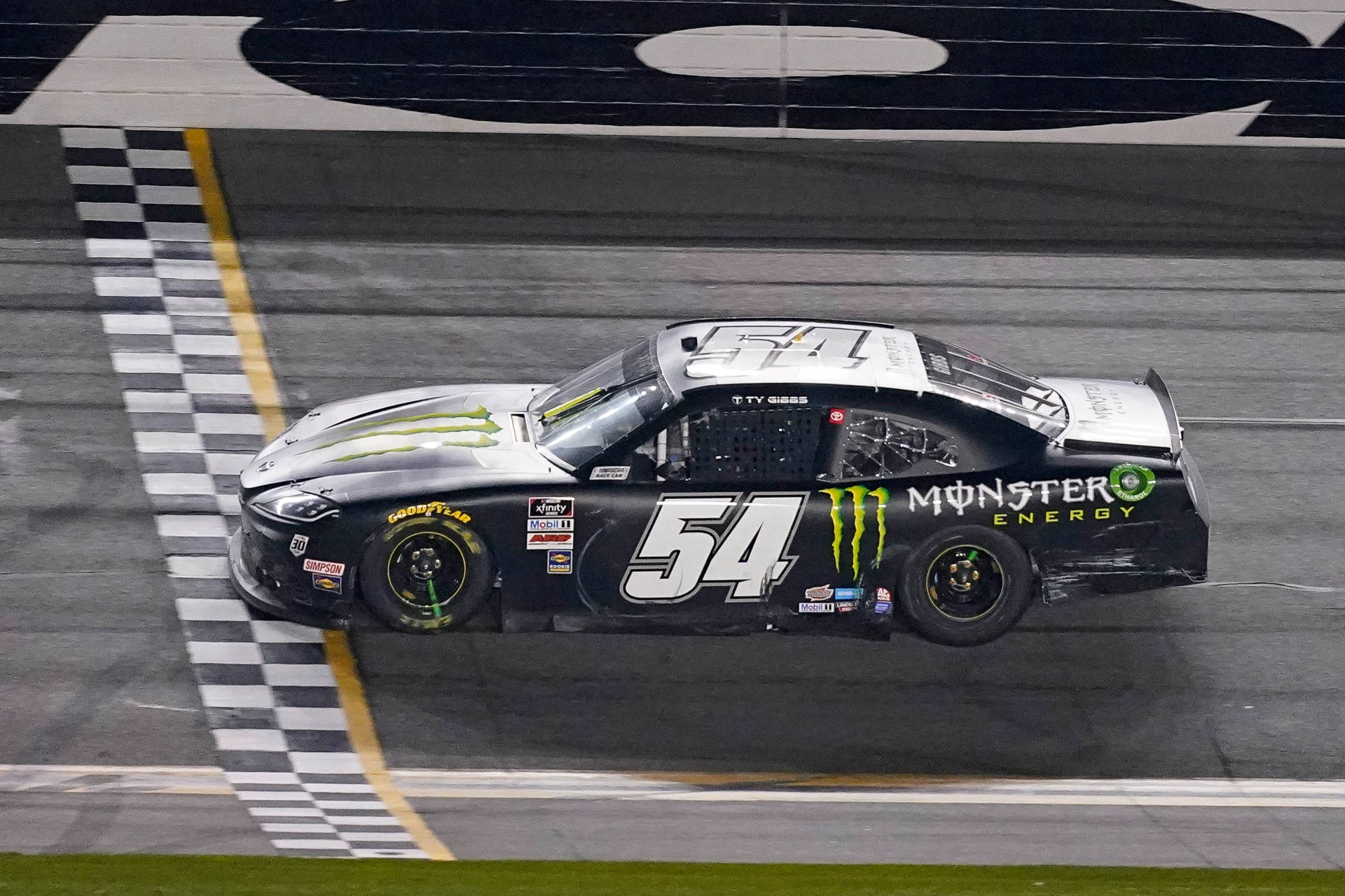 黑色 NASCAR 賽車在夜間越過終點線，帶有格仔旗。