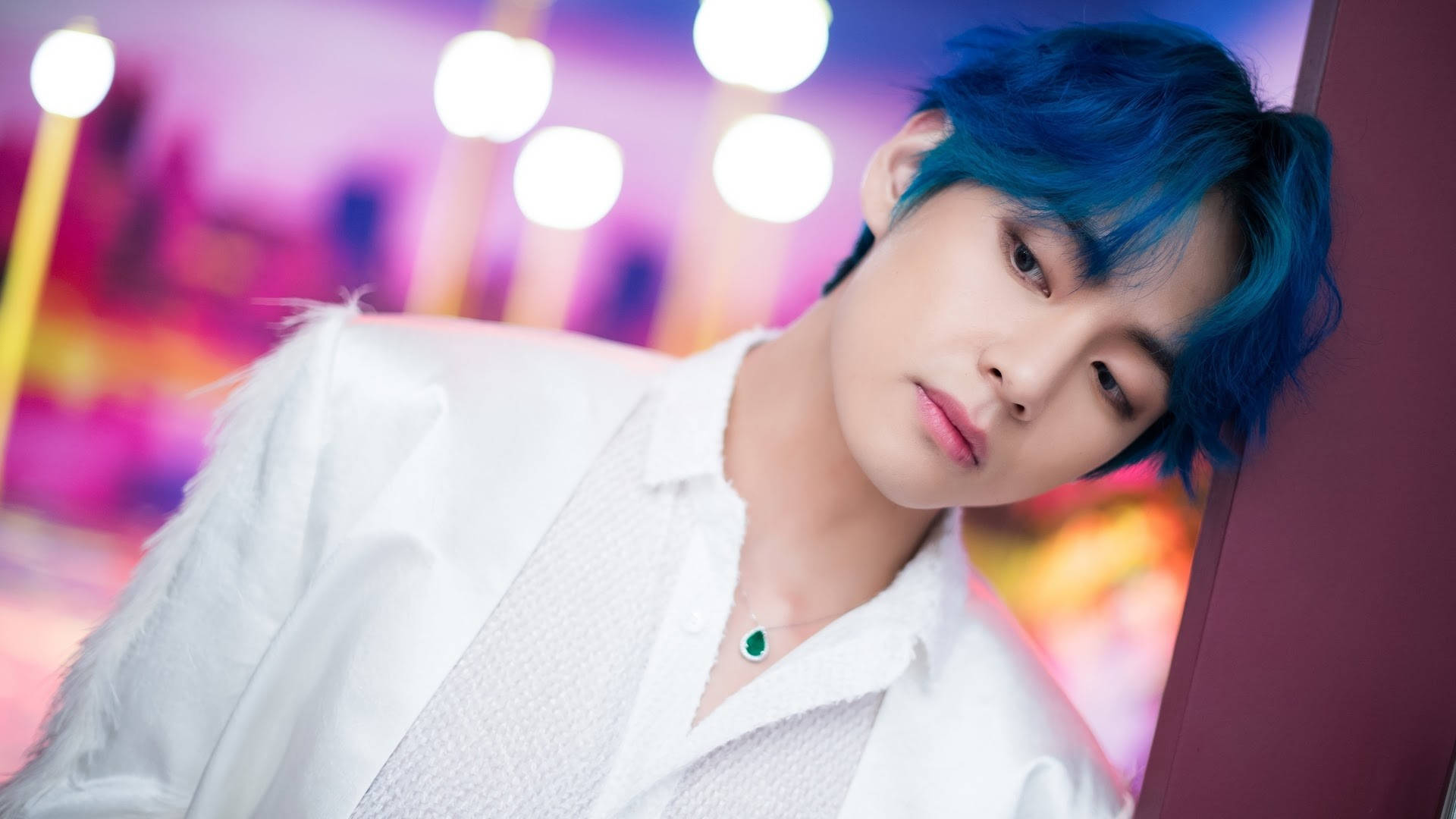 泰亨《Boy With Luv》 壁紙 — 一位擁有鮮豔藍色頭髮的年輕男子，穿著白色紋理襯衫，在彩色散景燈光下靠著牆。