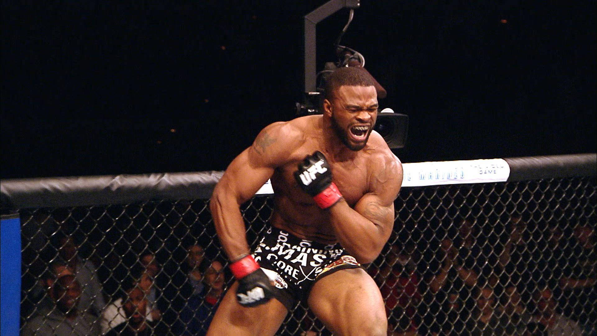 泰倫·伍德利原始慶祝 壁紙 — 一位肌肉發達的鬥士在UFC八角籠內勝利咆哮，背景有觀眾觀看。