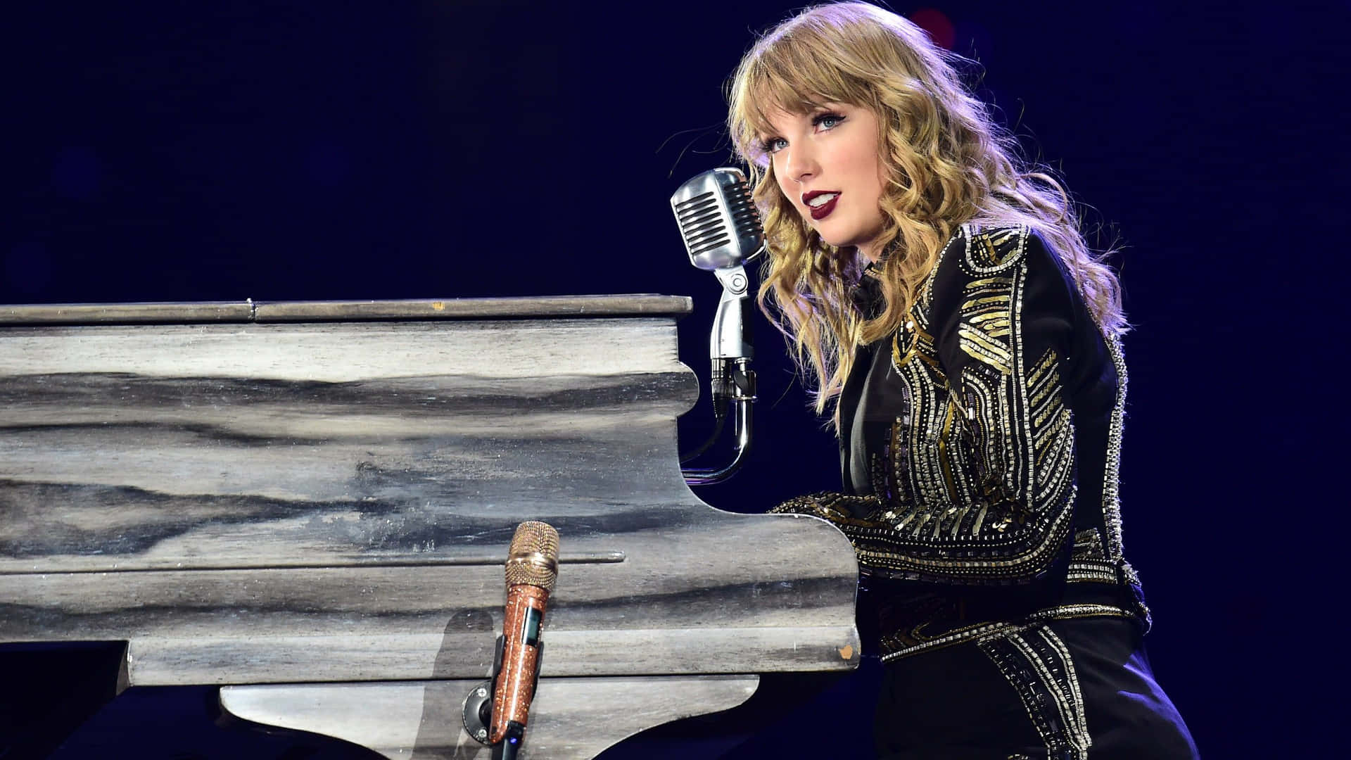 Taylor Swift 在舞台上用復古咪高峰在鋼琴前唱歌。