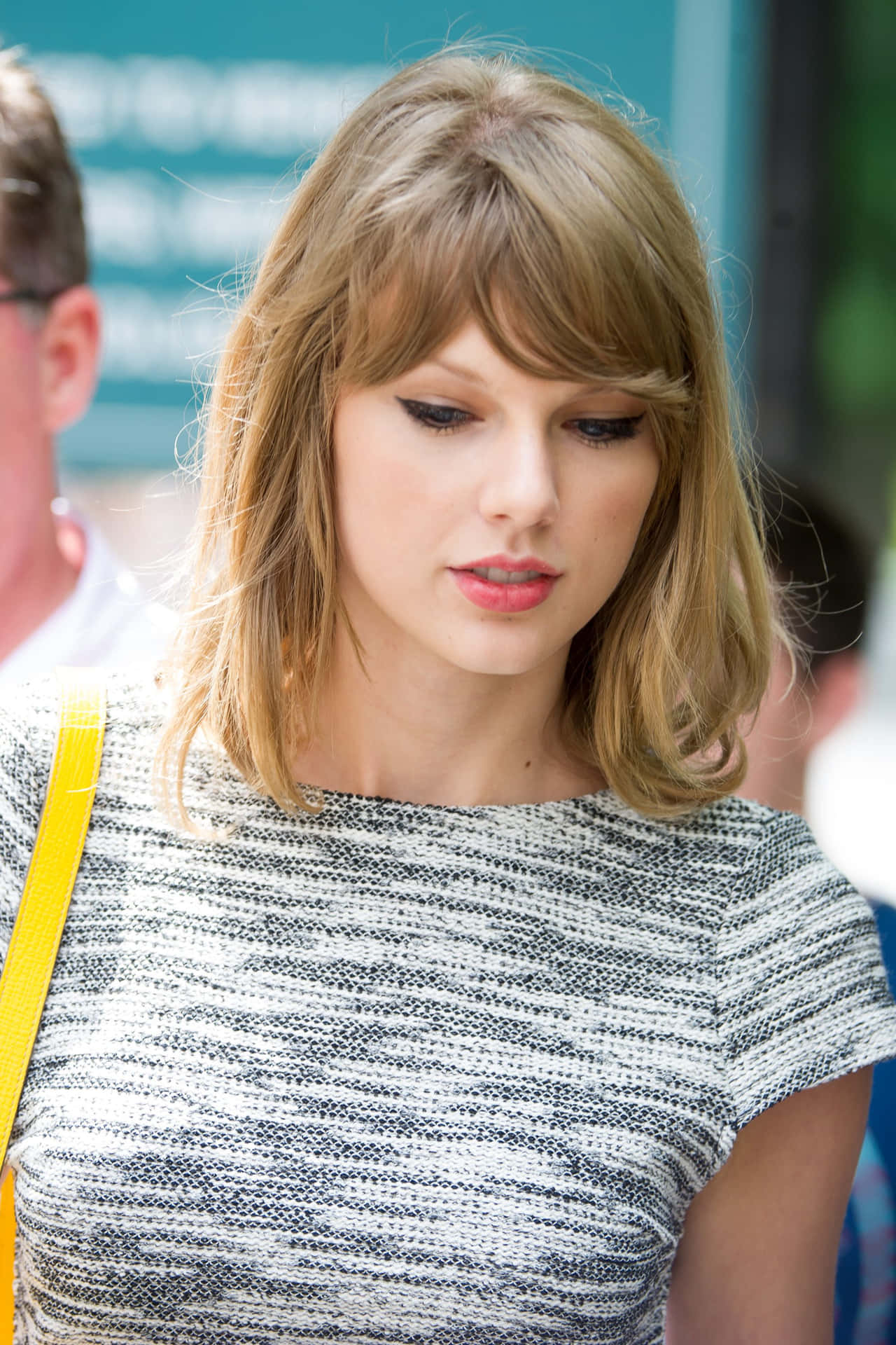 Taylor Swift 身穿灰色質感上衣，搭配黃色肩帶手袋，在戶外。