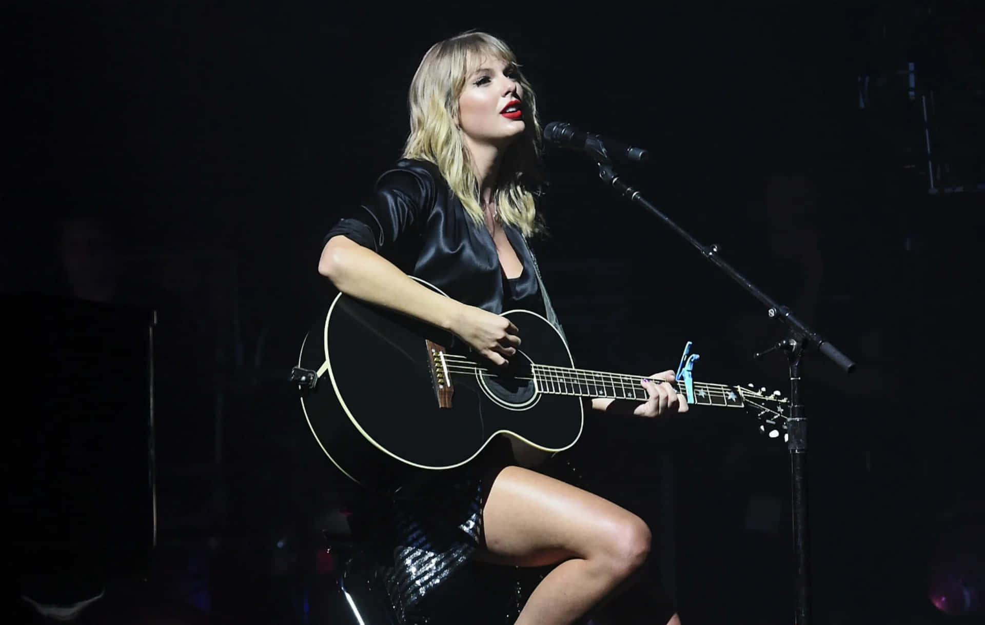Taylor Swift 在舞台上邊彈黑色木結他邊對著咪高峰唱歌。