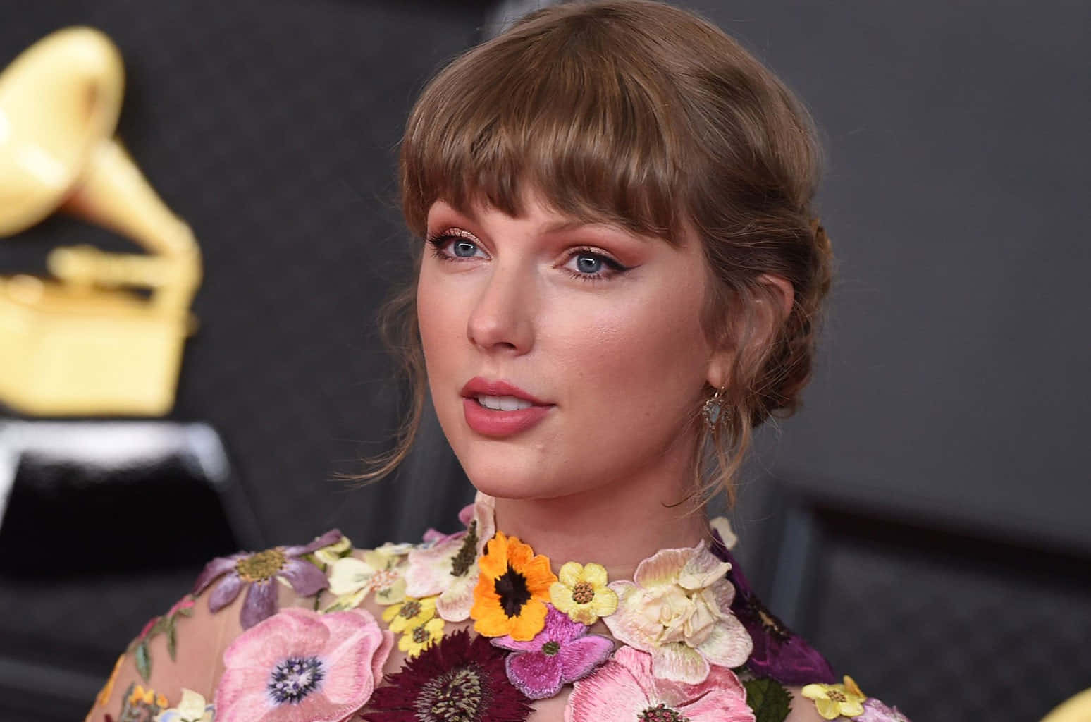 Taylor Swift 在格林美獎頒獎禮上身穿花卉裙，背景有金色獎盃。