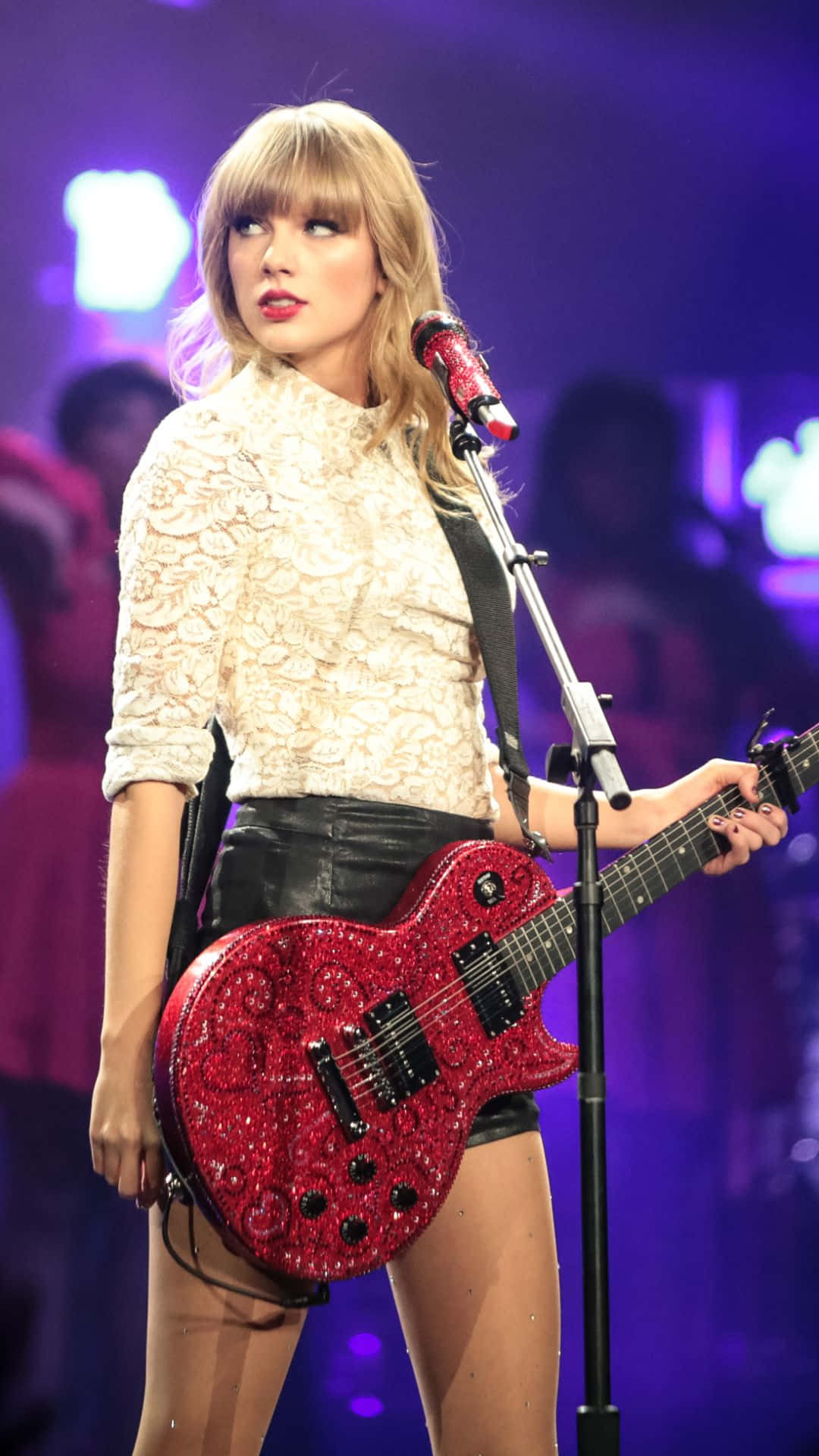 Taylor Swift 在紫色燈光舞台上彈奏紅色閃亮結他。