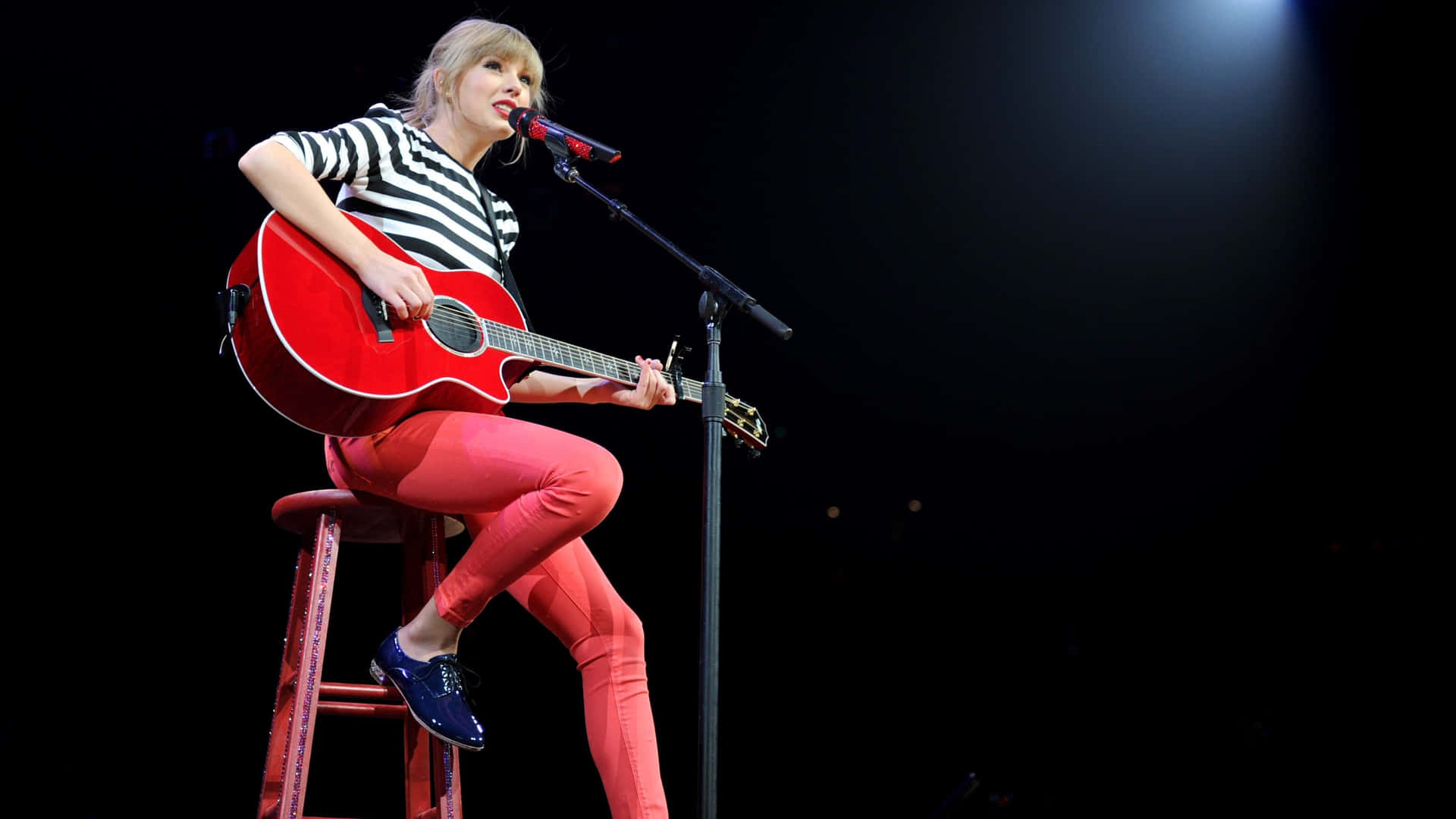 Taylor Swift 在舞台上邊彈紅色結他邊對著咪高峰唱歌。