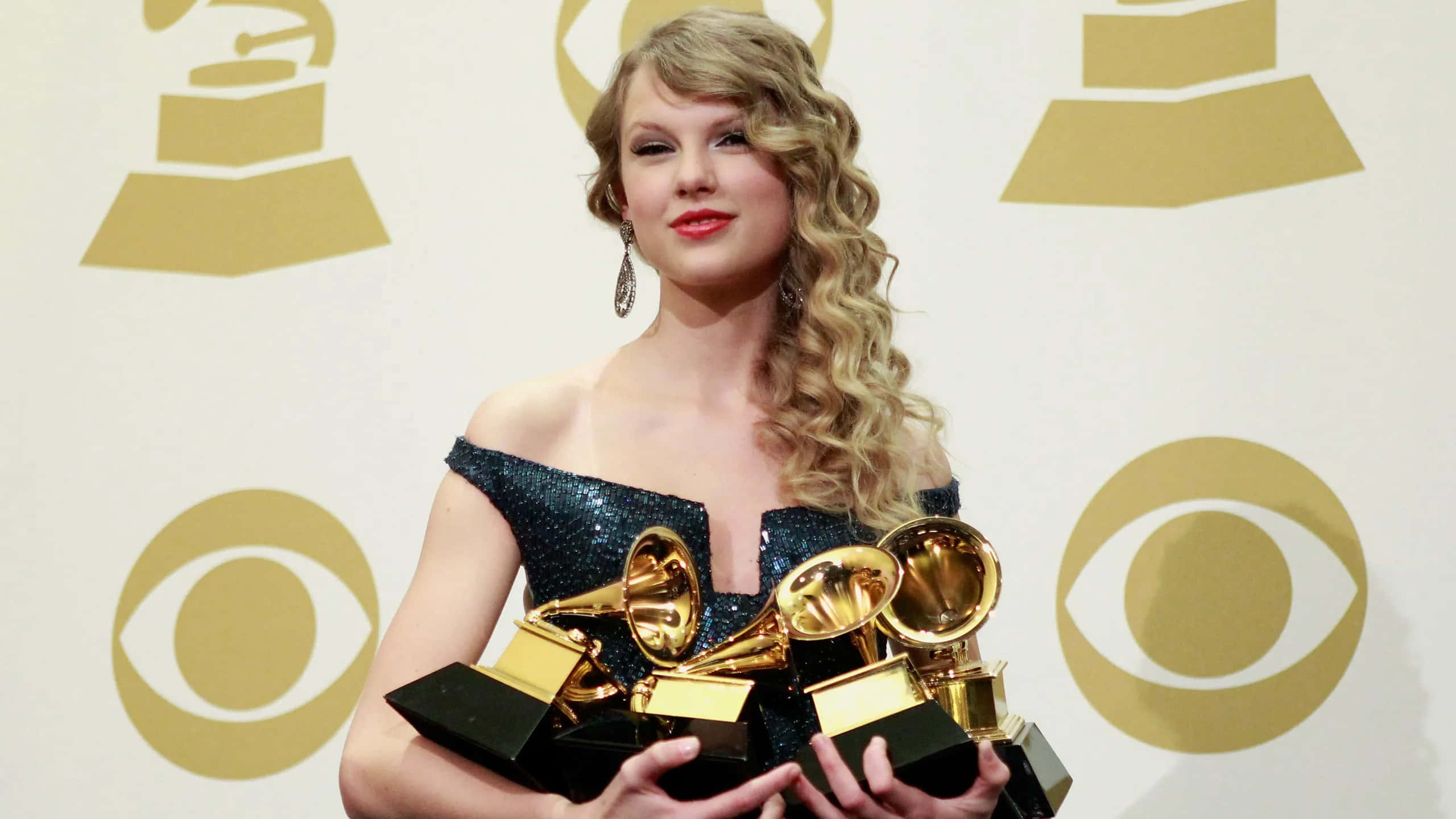 泰勒·斯威夫特獲格萊美獎經典畫面 壁紙 — Taylor Swift 微笑著手持多個格林美獎，背景為金色標誌。