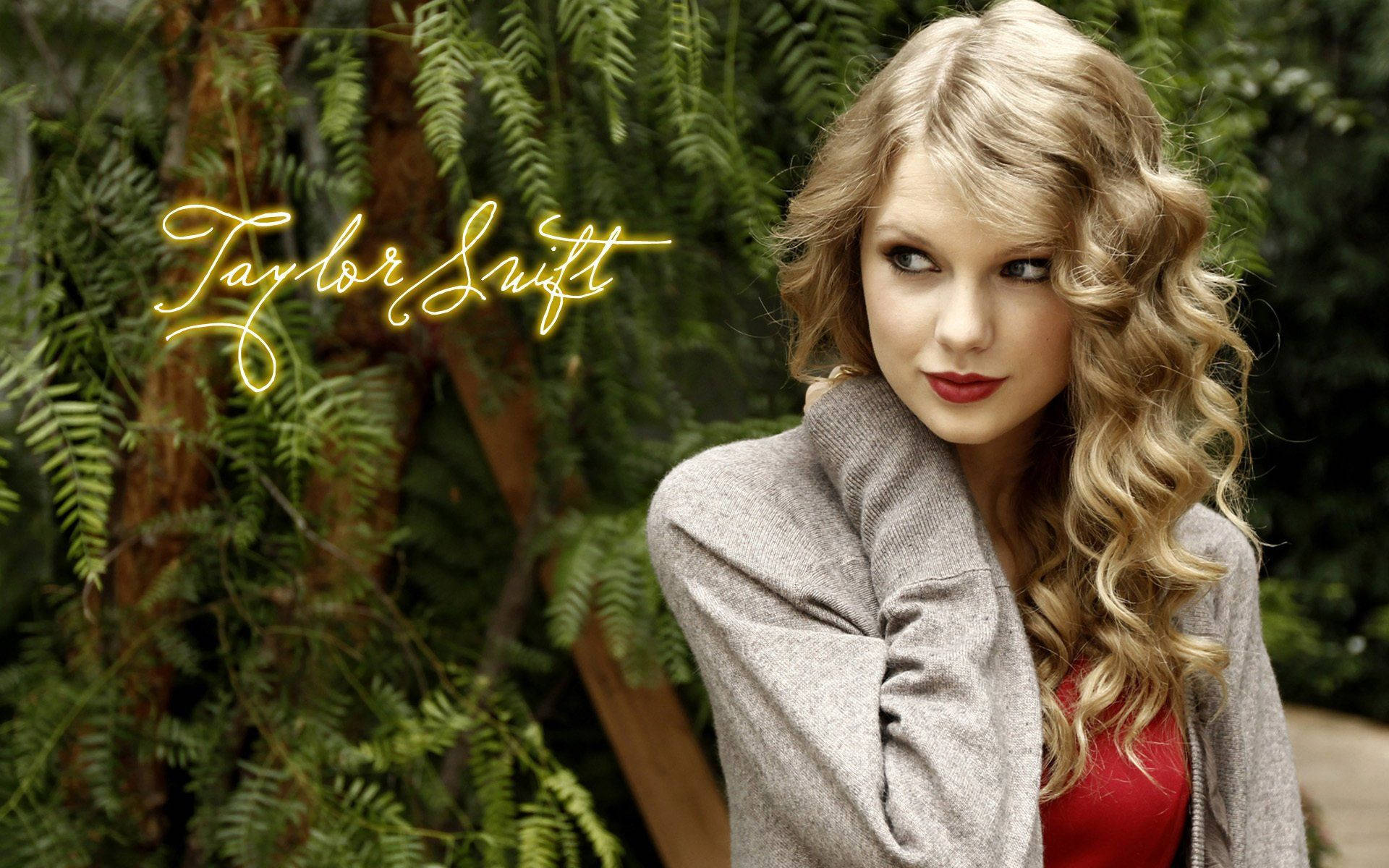 Taylor Swift 身穿灰色外套和紅色上衣，站在蕨類植物中，帶有發光名字文字。