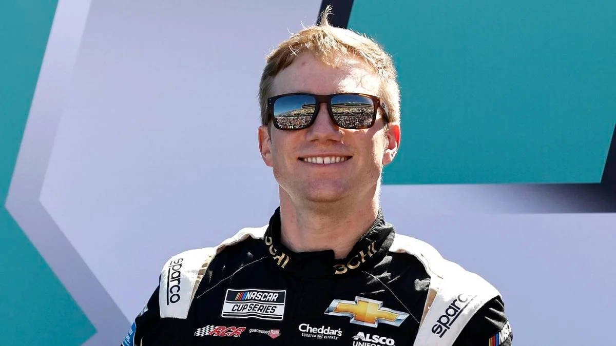 NASCAR車手身穿賽車服微笑，太陽眼鏡反射體育場。