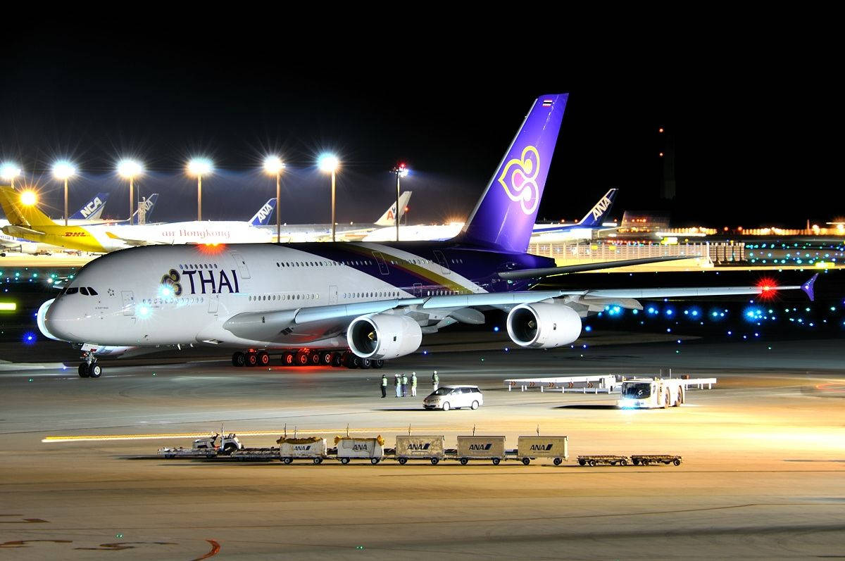 泰國航空A380飛機在夜間機場停機坪上，有地勤人員和行李車。