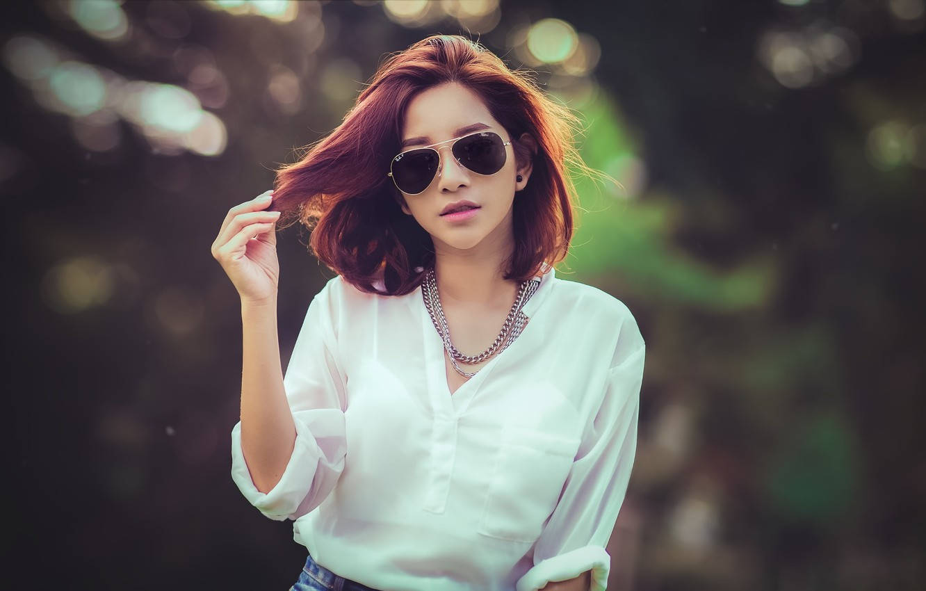 一位紅髮女性戴著太陽眼鏡，穿著白色襯衫在戶外。