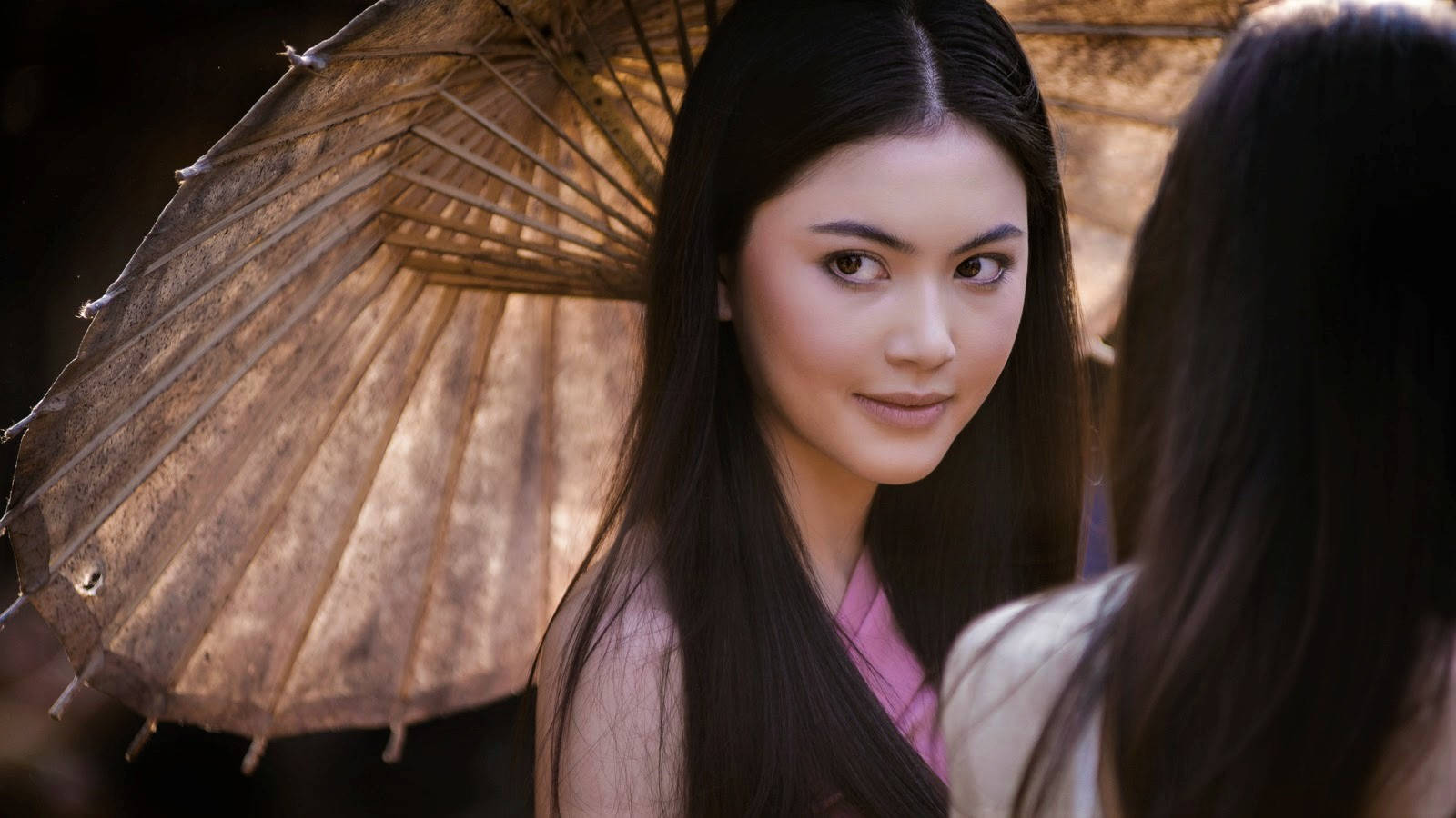手持傳統傘的女性在溫暖光線中凝視另一個人