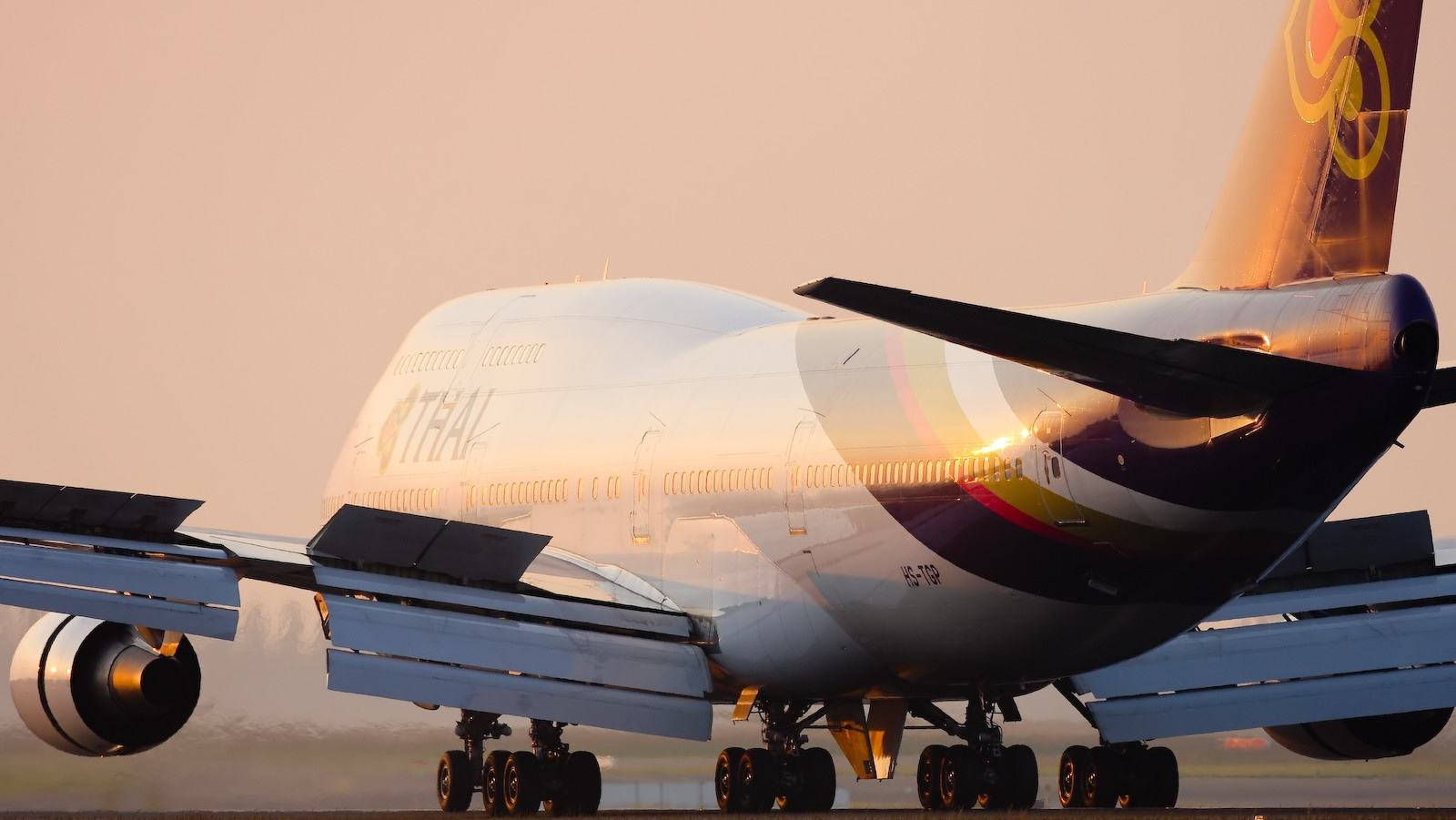 泰國航空珍寶客機在夕陽下滑行，金色光線反射在機身上
