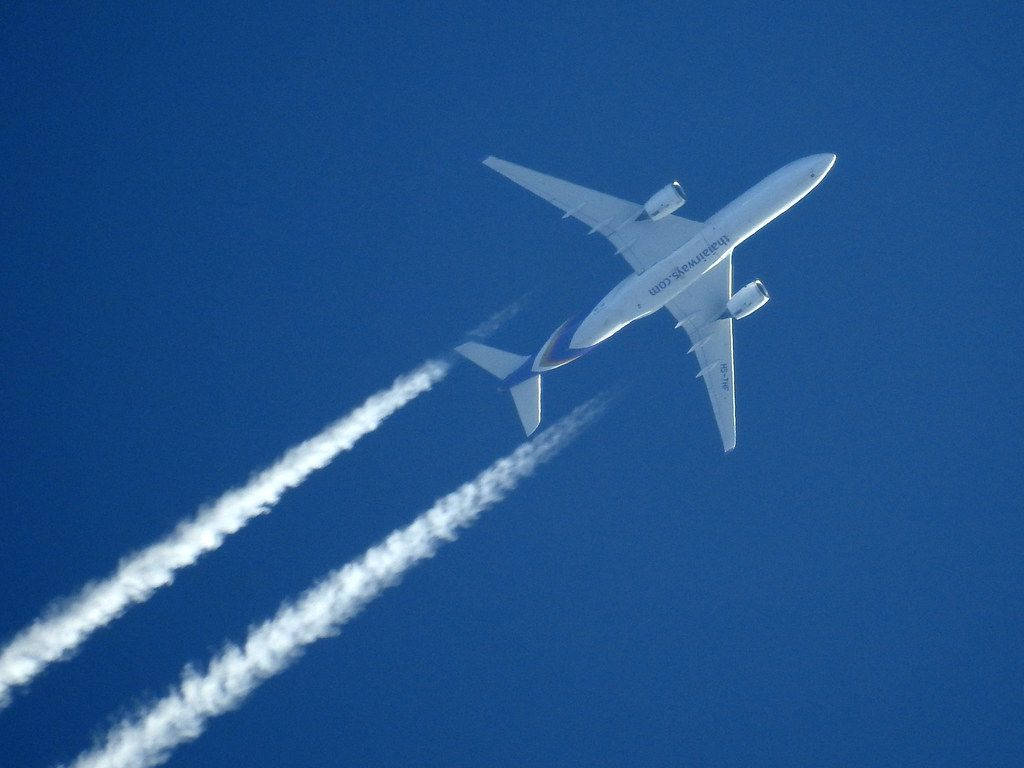 白色阿聯酋航空飛機在藍天中高飛，帶有白煙