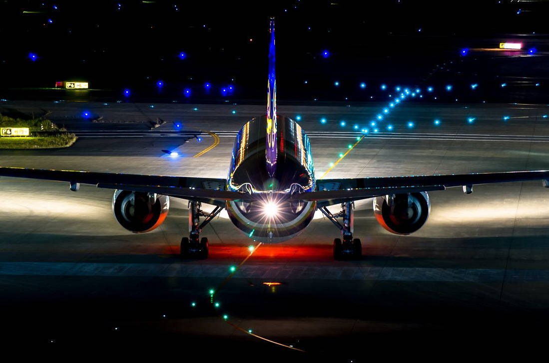 夜間在黑暗的跑道上，一架大型飛機被自身燈光照亮。