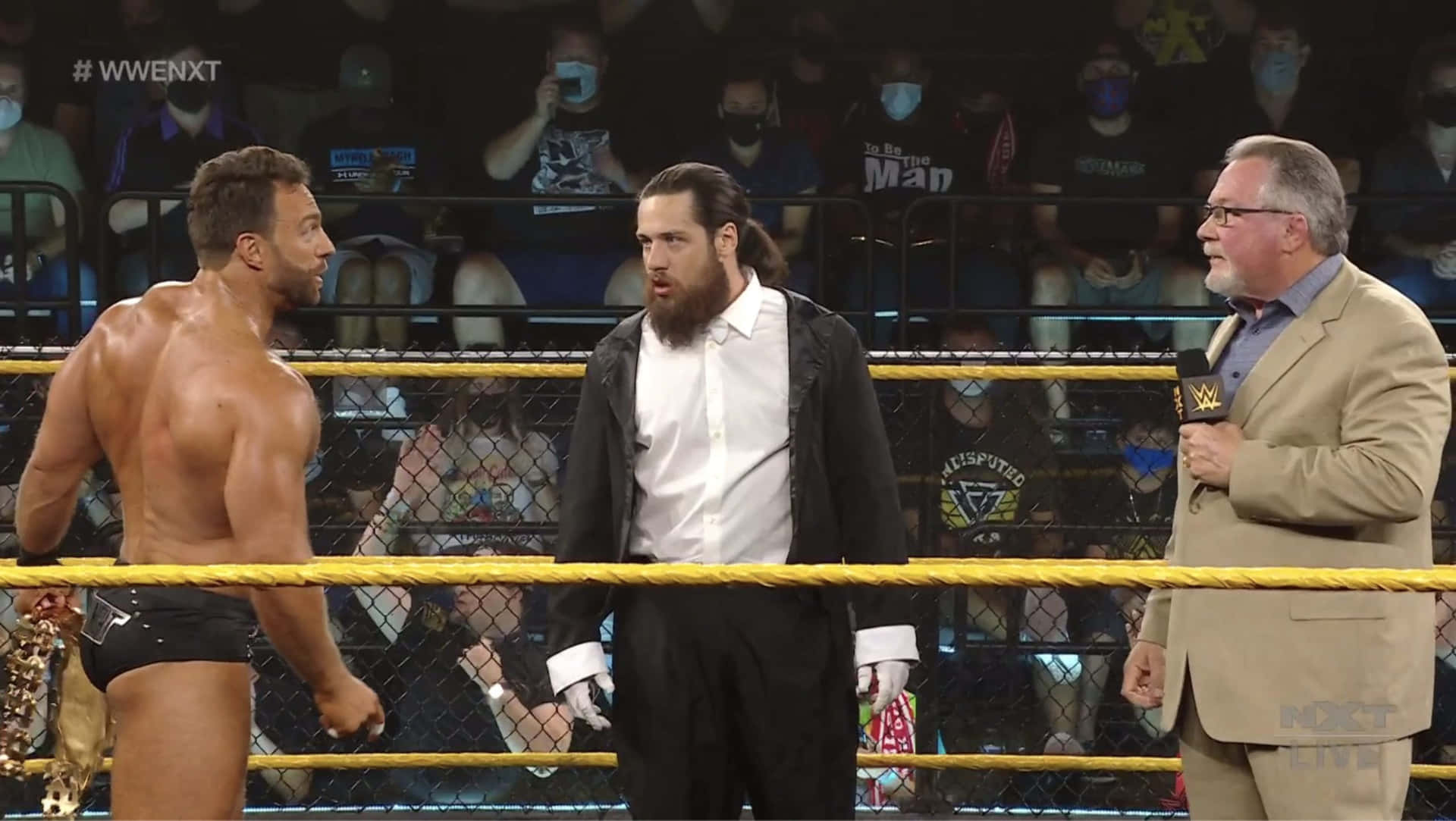 WWE NXT摔角手和評論員在擂台上，觀眾戴著面具。
