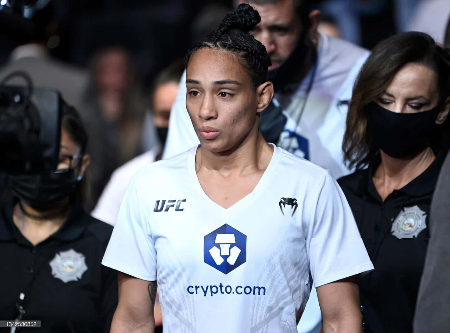 身穿白色球衣的女性UFC拳手在體育賽事中經過保安人員。
