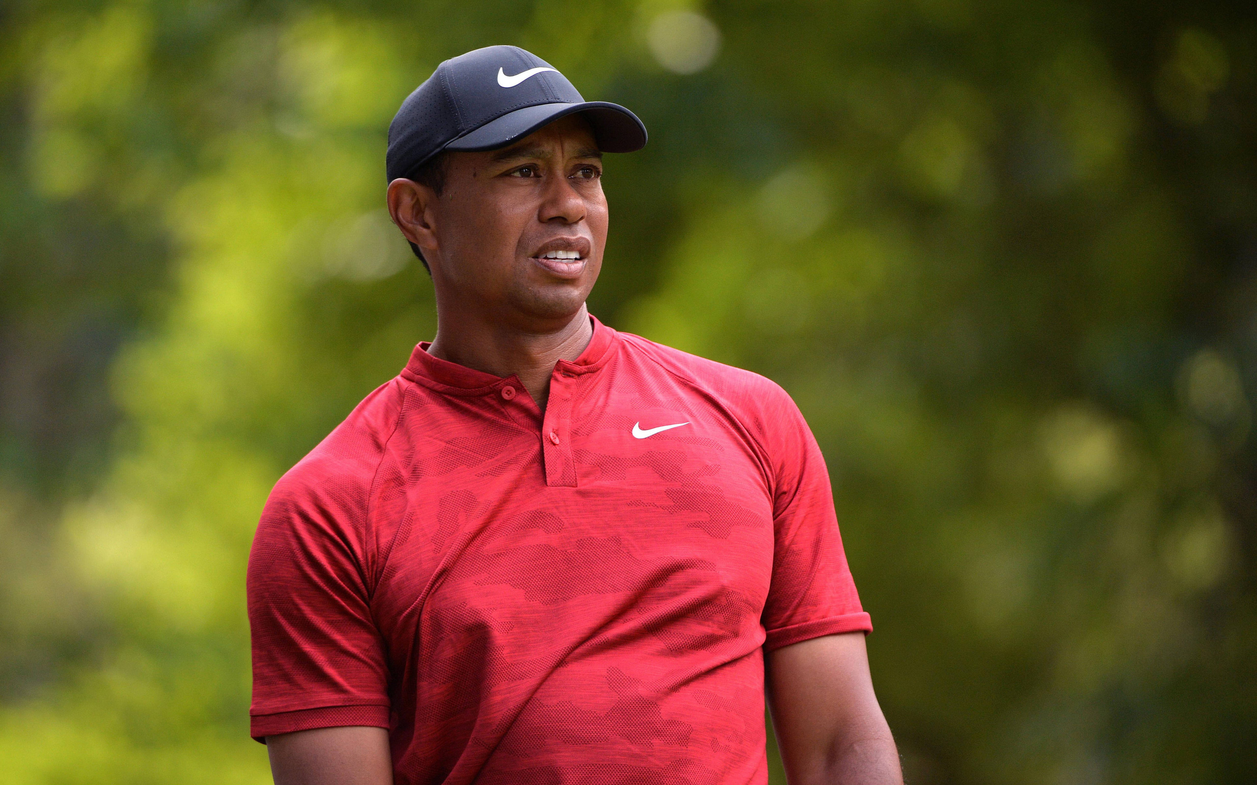泰格·伍茲 2019 WGC墨西哥錦標賽 壁紙 — 老虎活士穿著紅色Nike Polo衫和帽子，專注地站在模糊的綠色樹葉背景前。