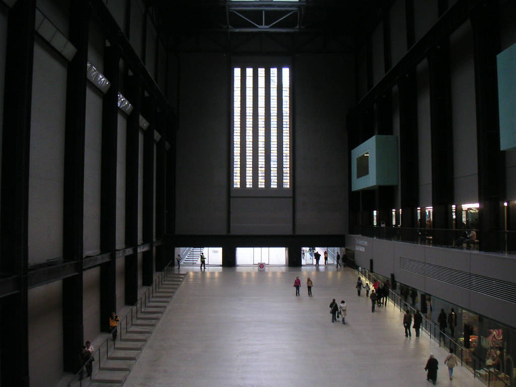 泰特現代藝術館渦輪廳內景 壁紙 — 寬敞的現代博物館大廳，高聳的黑色橫樑和高大的垂直窗戶將明亮的光線投射在拋光地板上，散落的遊客在其中漫步。