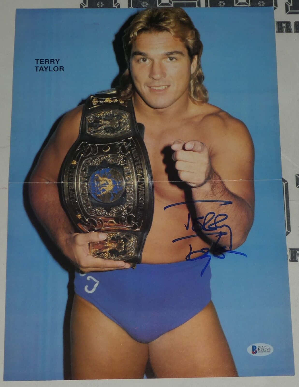 摔角手 Terry Taylor 身穿藍色短褲，手持帶有簽名的冠軍腰帶。