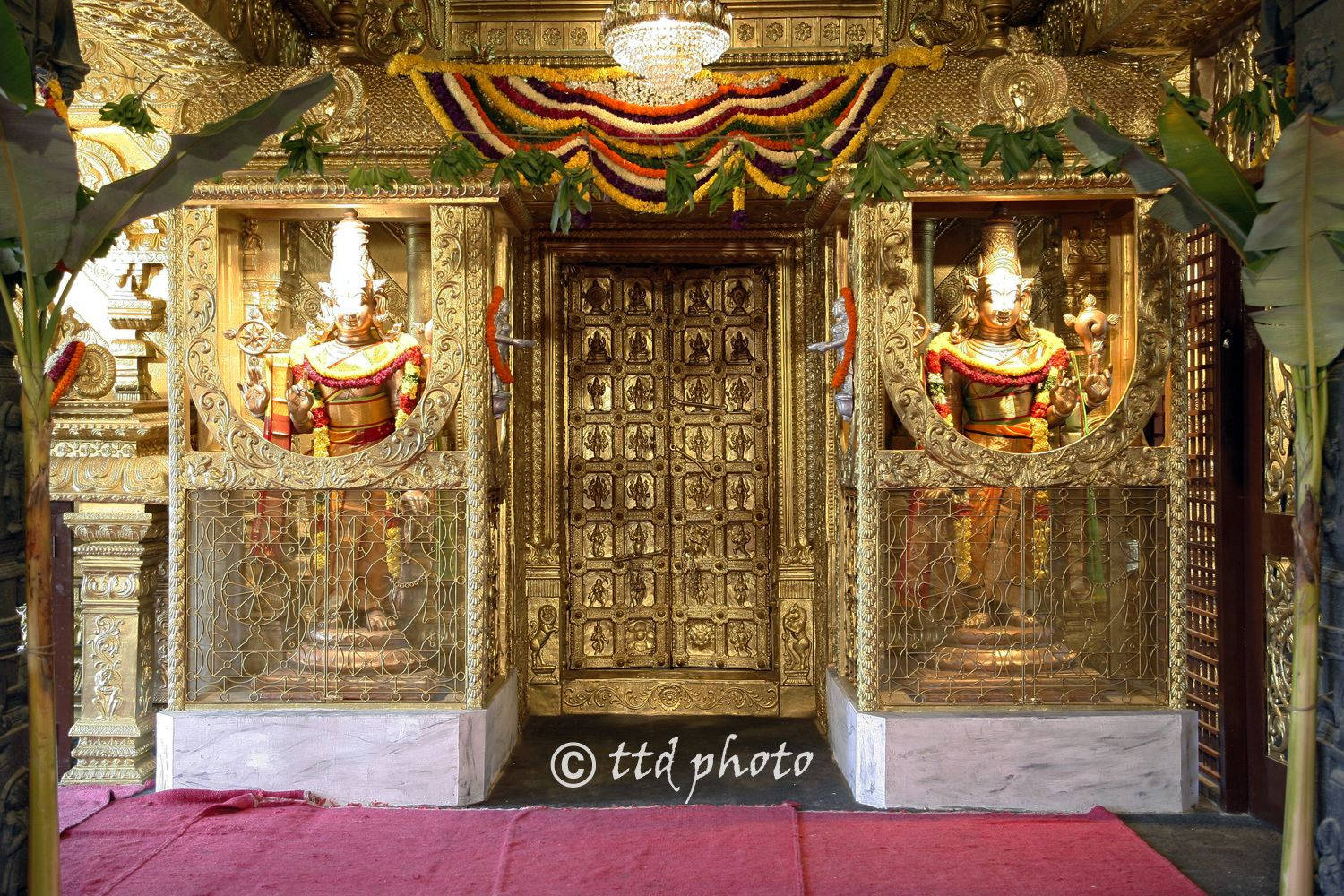 金色寺廟門口，有神像和花卉裝飾。