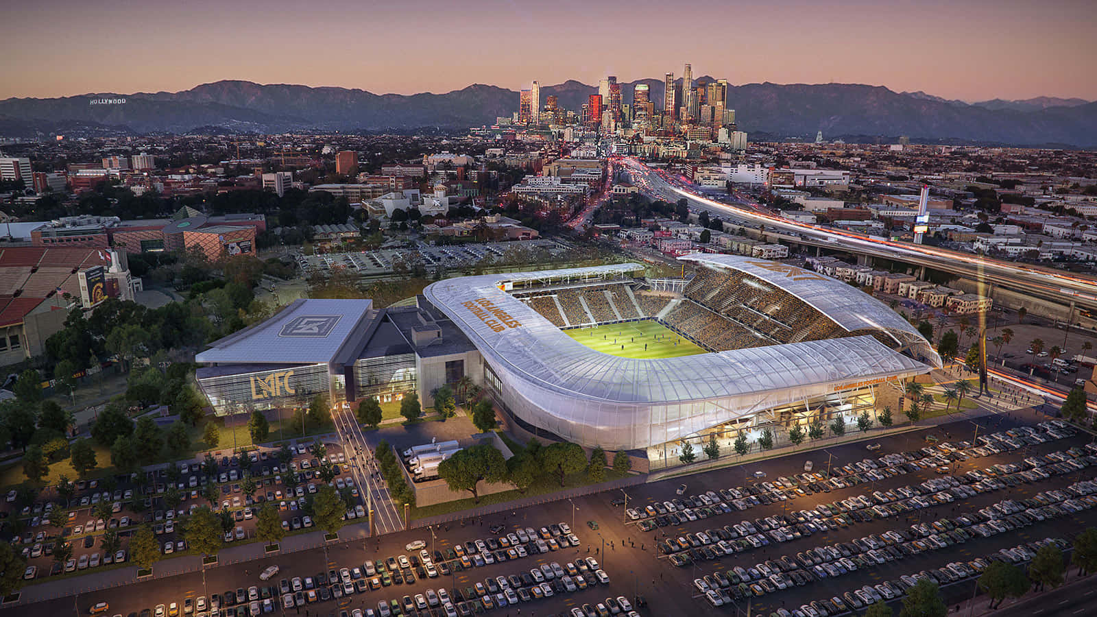 洛杉磯FC Banc of California體育館 壁紙 — 一個未來風格的體育場在黃昏時分發光，背景是城市燈光和山脈輪廓。