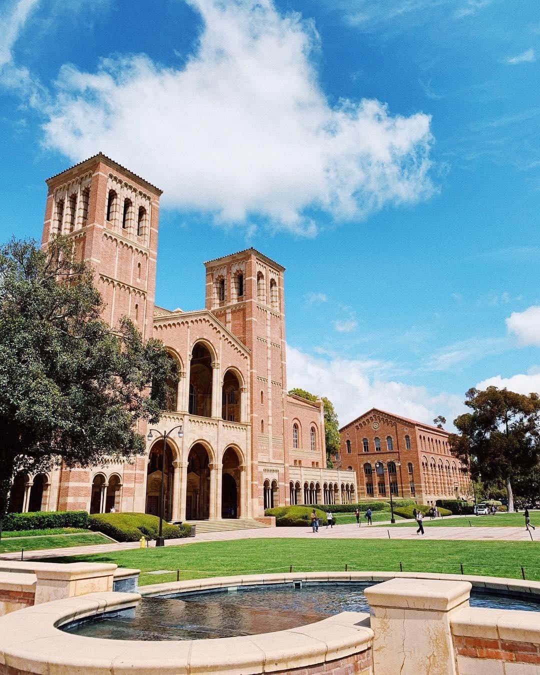 大學校園，有紅磚建築、綠色草坪和噴泉，在陽光明媚的天空下。