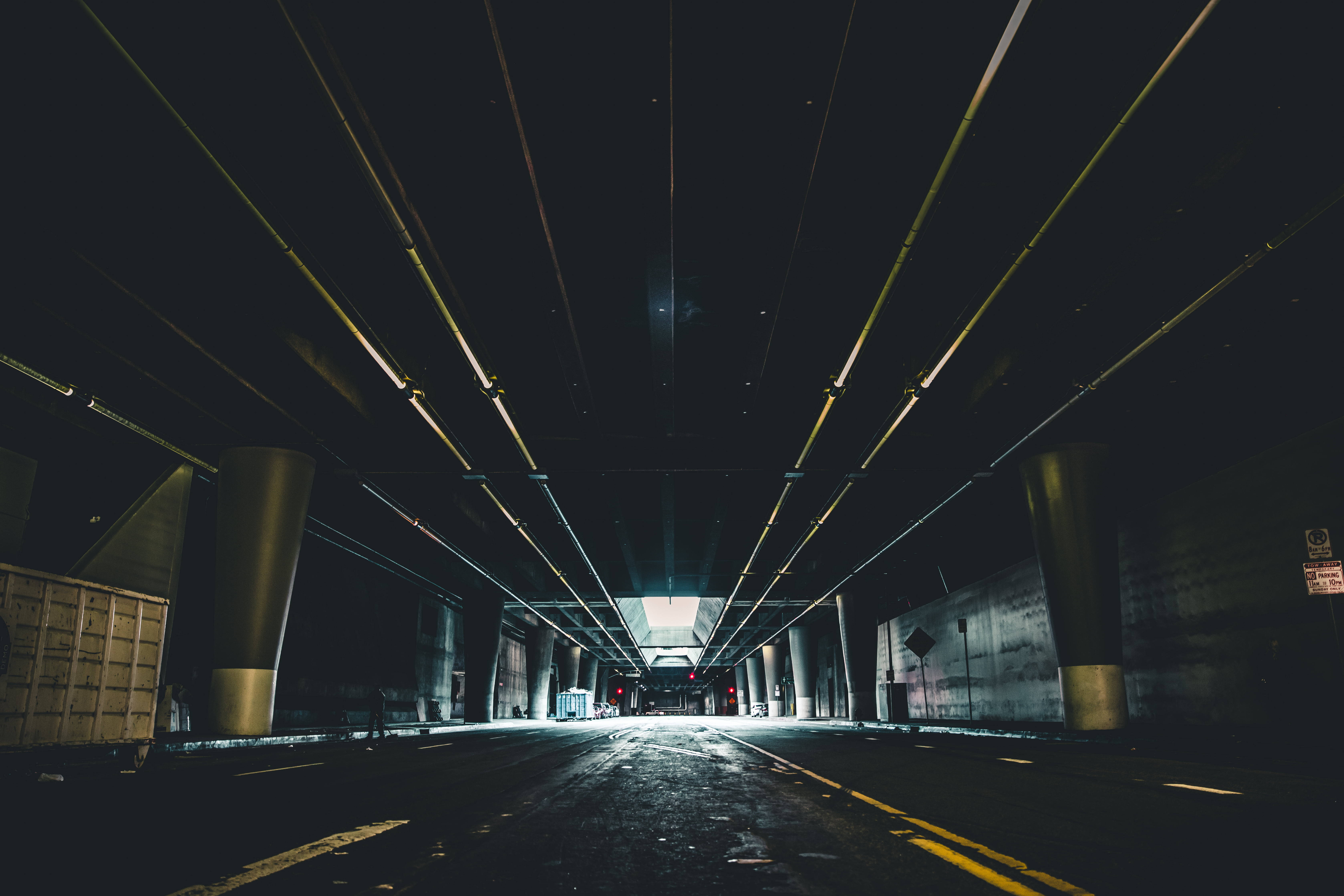 洛杉磯地下停車場 壁紙 — 一條長長的黑暗隧道，有發光的黃色燈光和混凝土柱，通往遠處明亮的出口。