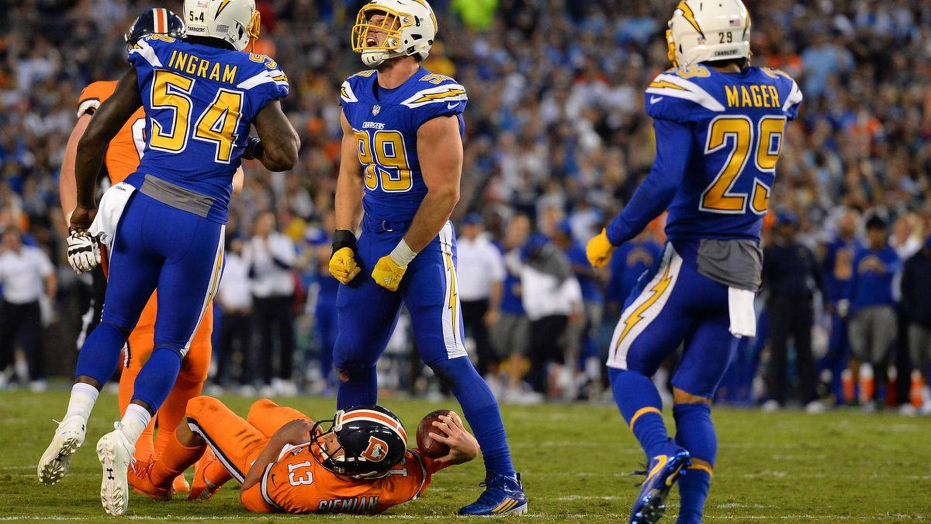 洛杉磯突襲者隊 NFL 賽事 壁紙 — 身穿藍色和橙色球衣的足球運動員在體育場燈光下，於充滿活力的綠色球場上慶祝達陣。