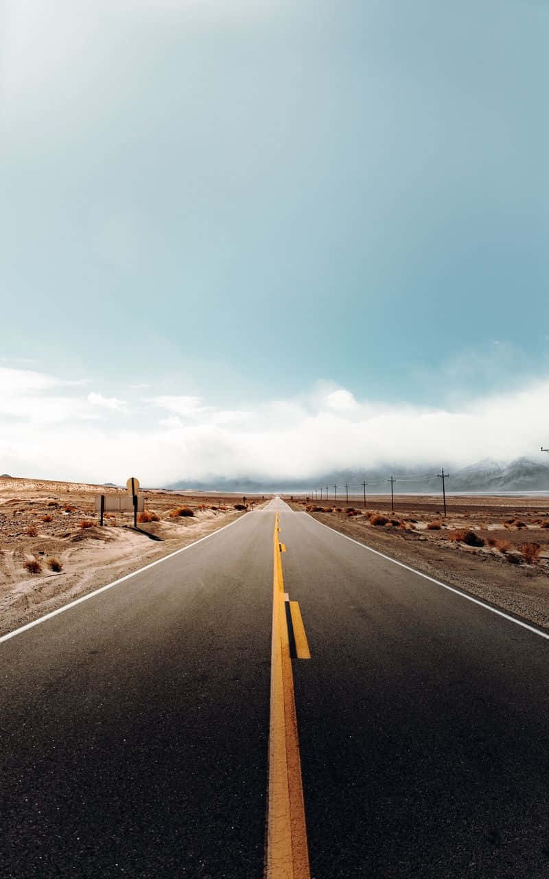 一條空蕩的公路穿過沙漠，在藍天下通往遠山。