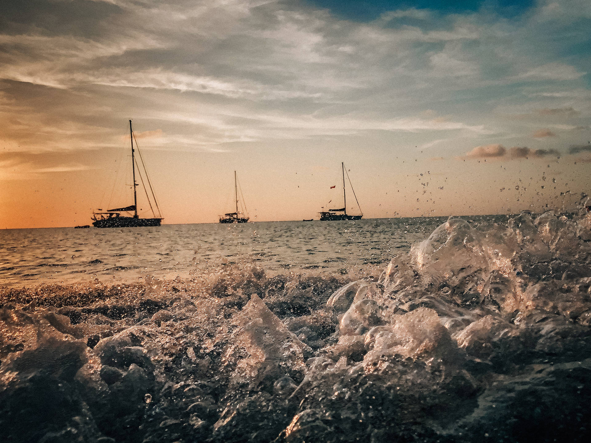 夕陽下浪花飛濺，平靜的海平線上有帆船。