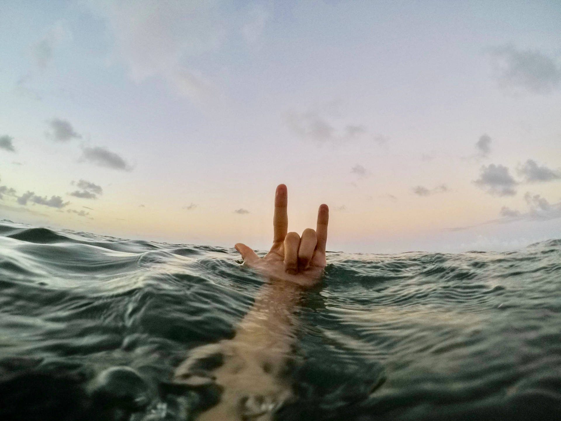 海水中手在日落時做出搖滾手勢