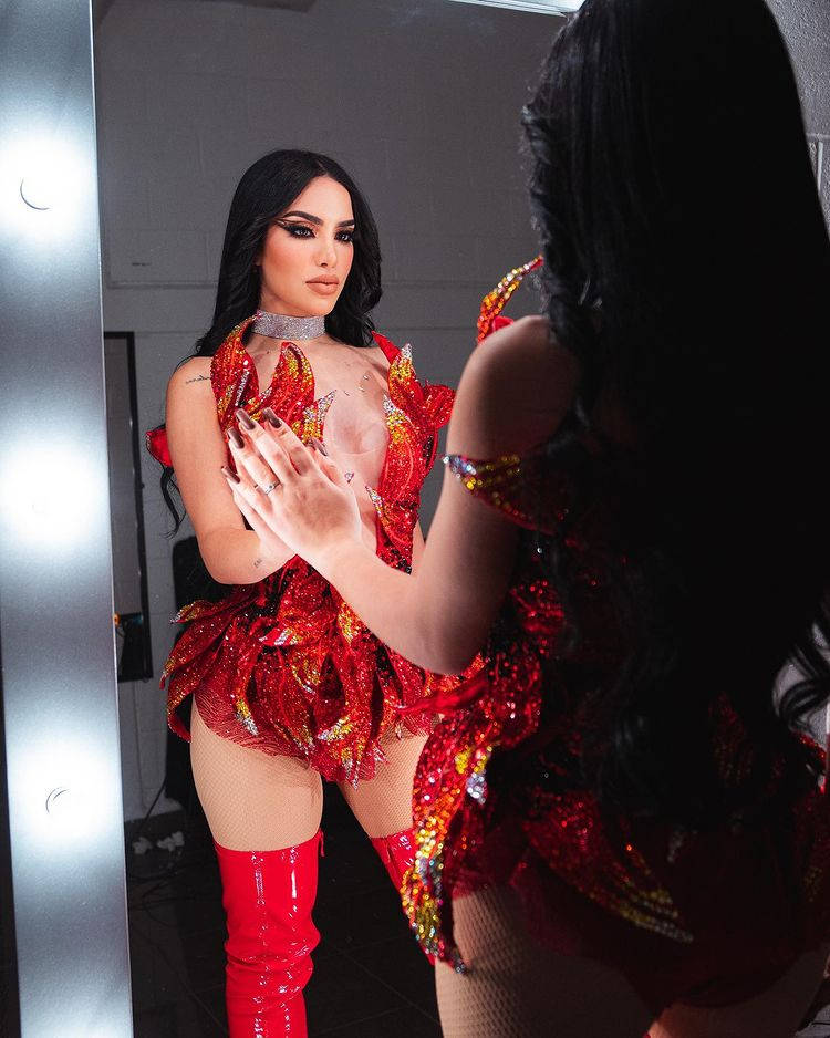活力四射的拉丁女歌手Kimberly Loaiza 壁紙 — 一位身穿閃亮紅色服裝的女性在明亮燈光下凝視後台鏡中的倒影。