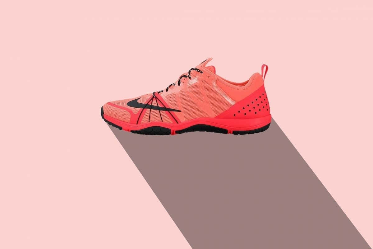 活力四射的紅色 Nike 運動鞋 – 靈動時尚 壁紙 — 一隻充滿活力的珊瑚色Nike訓練鞋在柔和的粉紅色背景上投下長長的陰影，呈現極簡數位藝術風格。