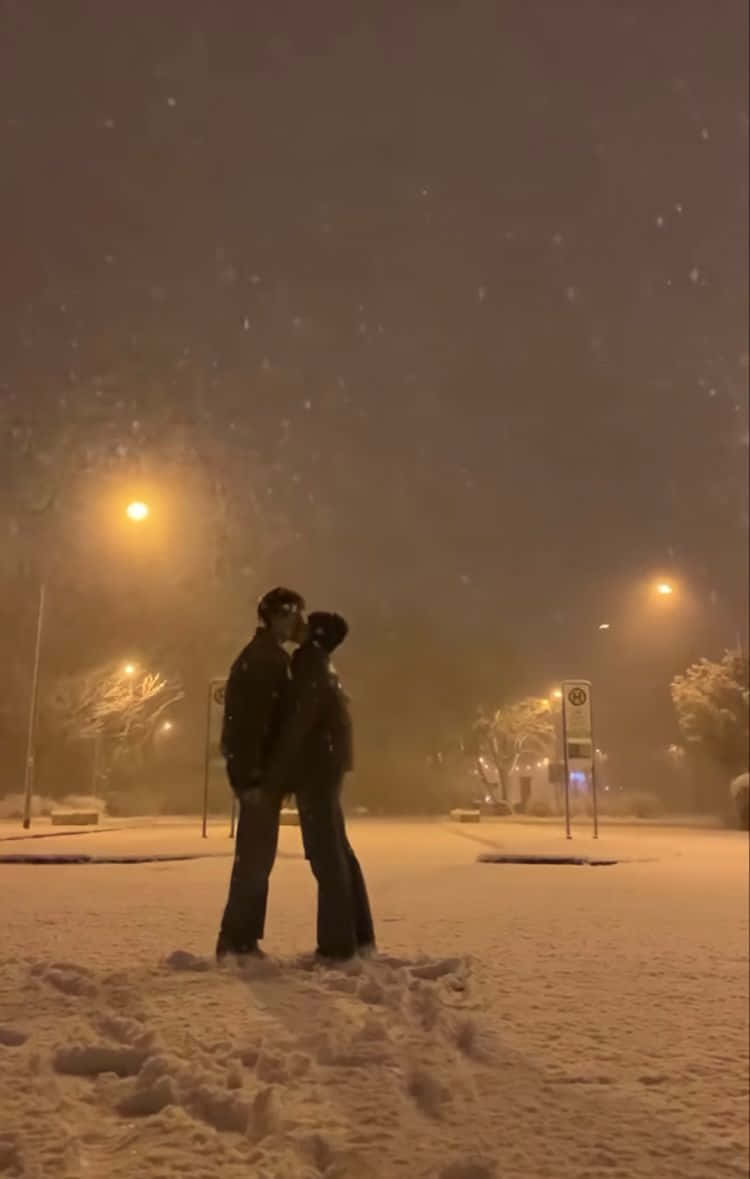一對情侶在夜晚的路燈下，於飄雪中親吻。