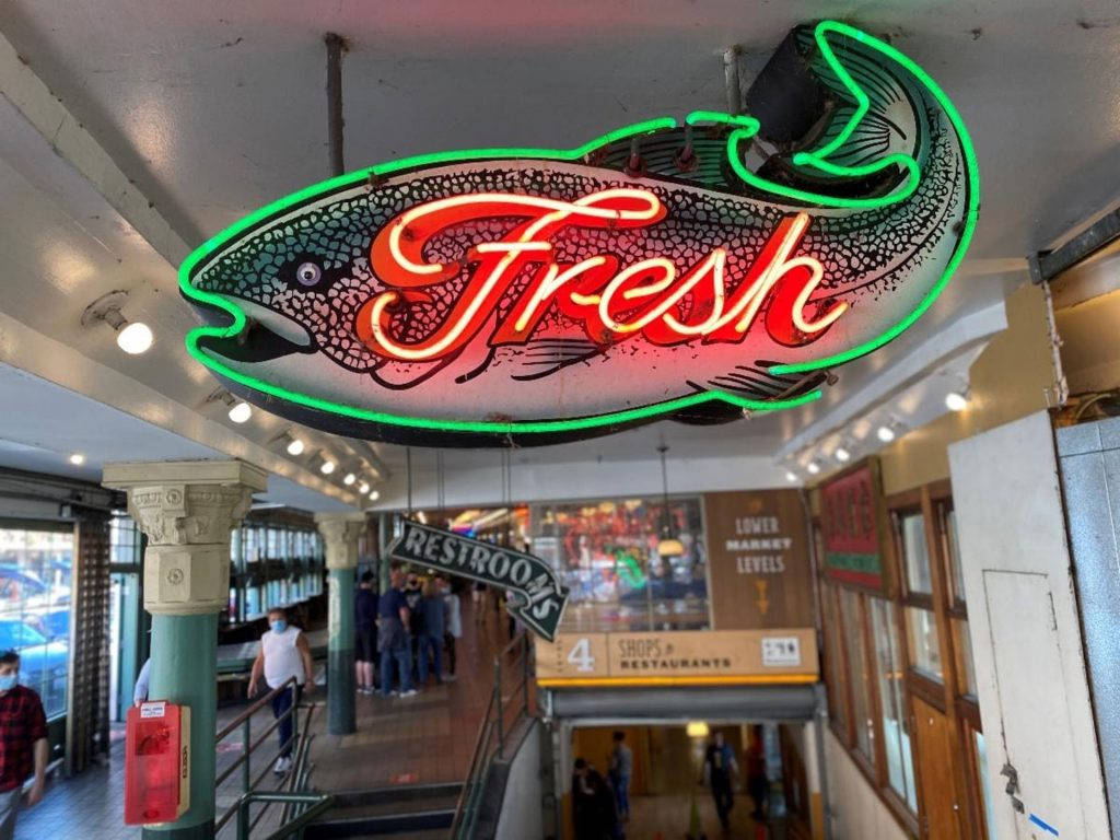 繁忙的室內市場中，一個寫著「Fresh」的魚形霓虹燈牌。