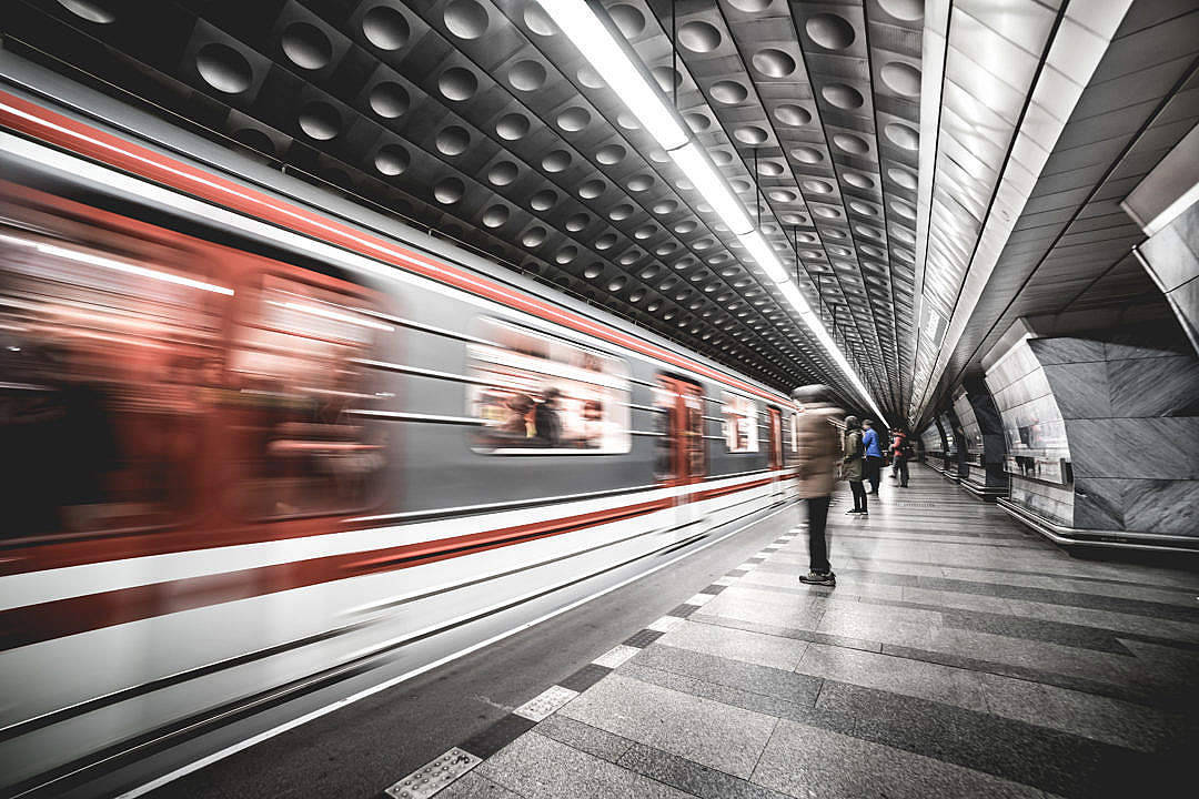 流動桌面載人列車 壁紙 — 一列高速行駛的紅色地鐵列車在一個時尚現代、鋪有幾何圖案瓷磚地板和圓形天花板燈的車站中，模糊地掠過一位孤獨等候的乘客。