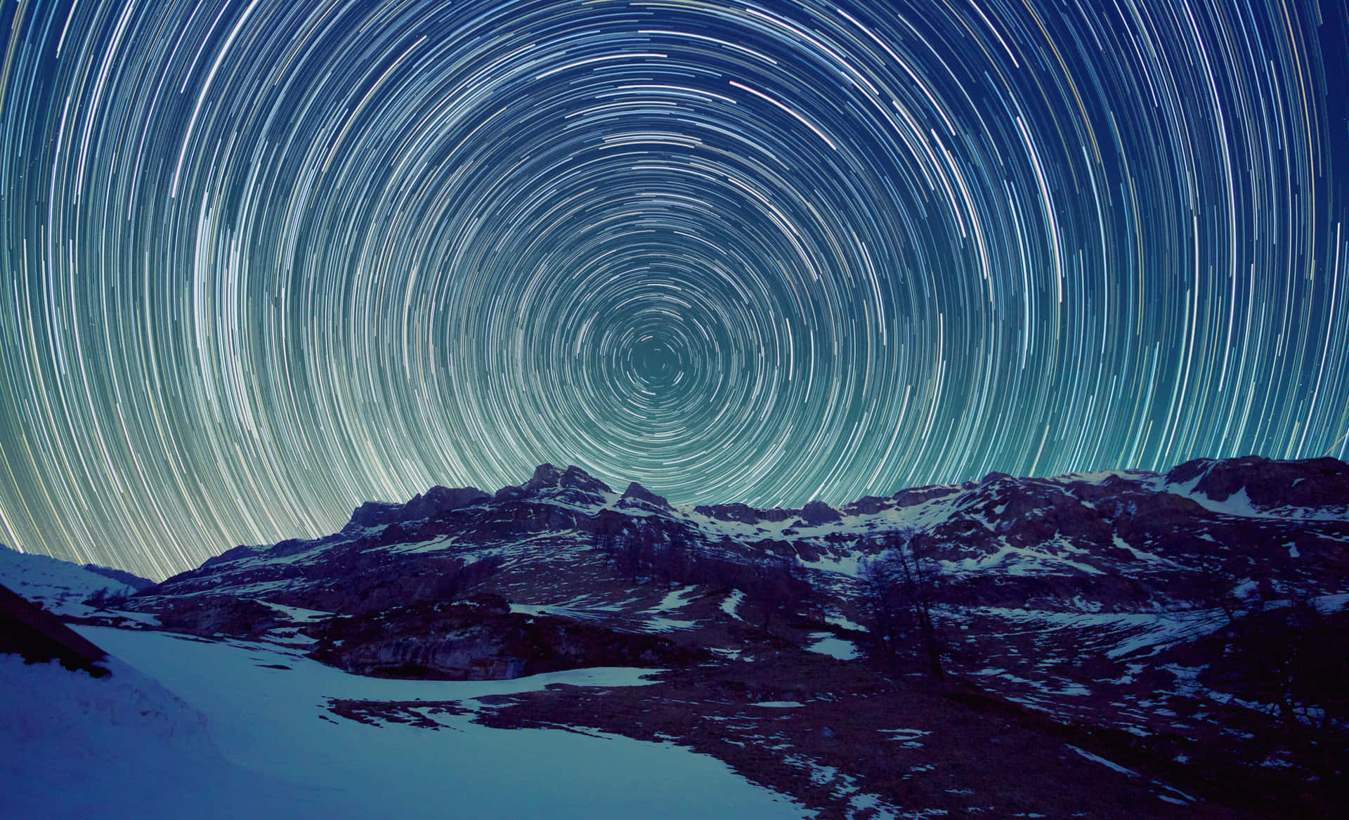 星軌在深藍色夜空下，在積雪的山脈上方旋轉。