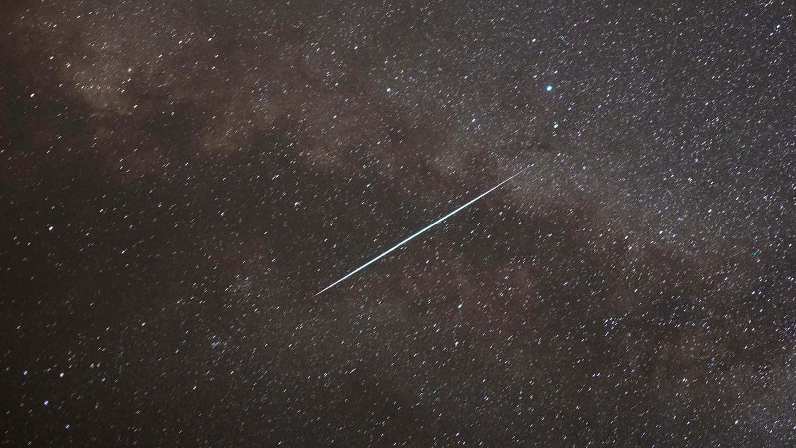 流星劃過夜空，璀璨奪目 壁紙 — 一顆明亮的流星斜斜劃過密集的星場，其中有黑暗的宇宙雲和散落的星星。