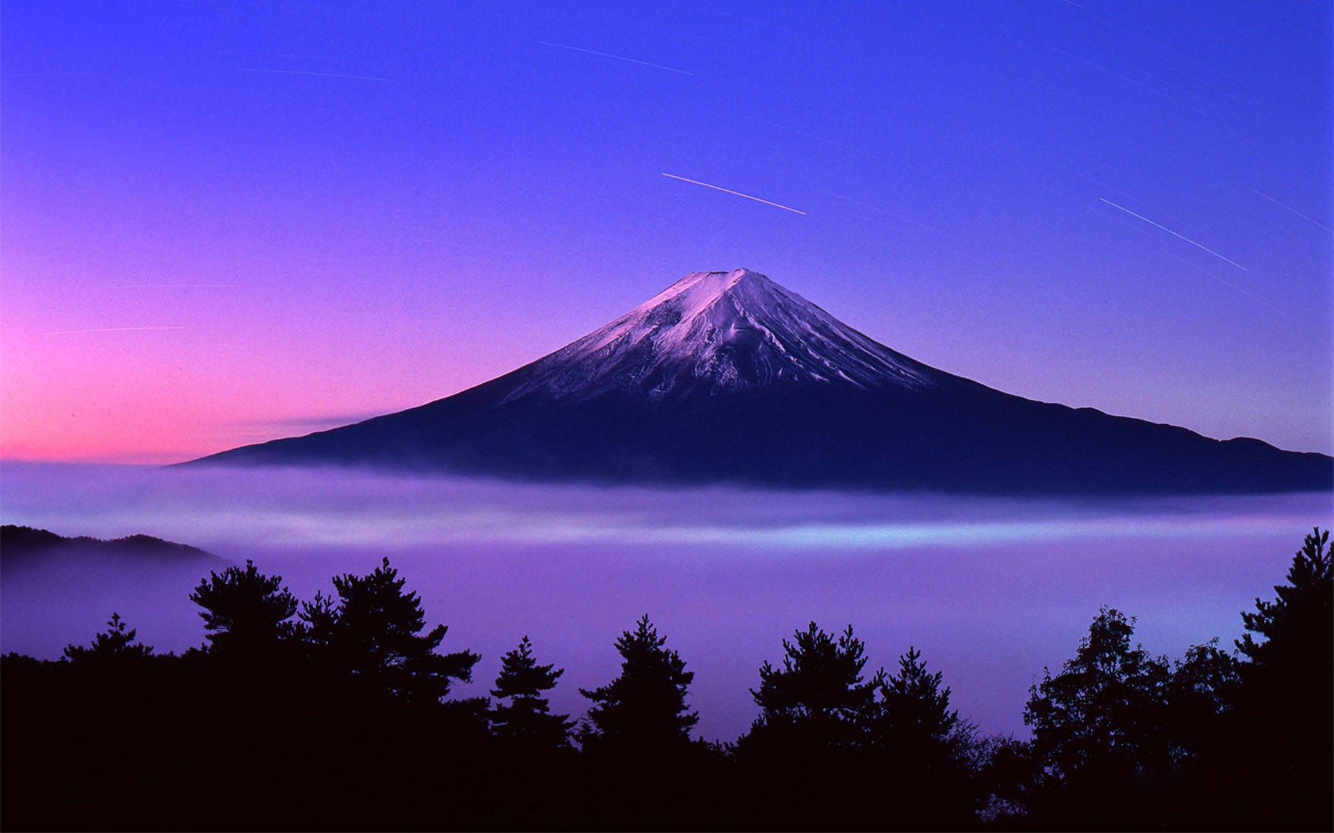 富士山在暮色中聳立於雲霧之上，天空呈現紫色和粉紅色。
