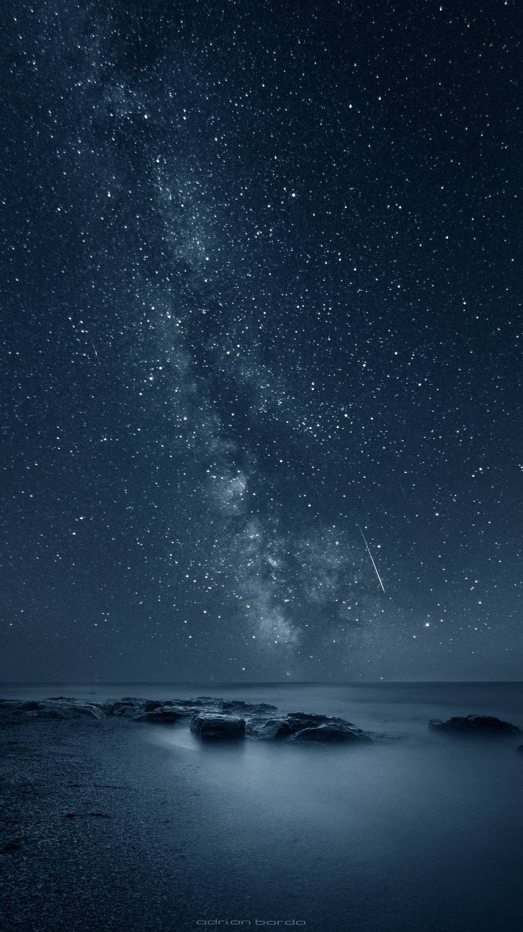 夜晚黑色海洋岩石上的銀河與流星