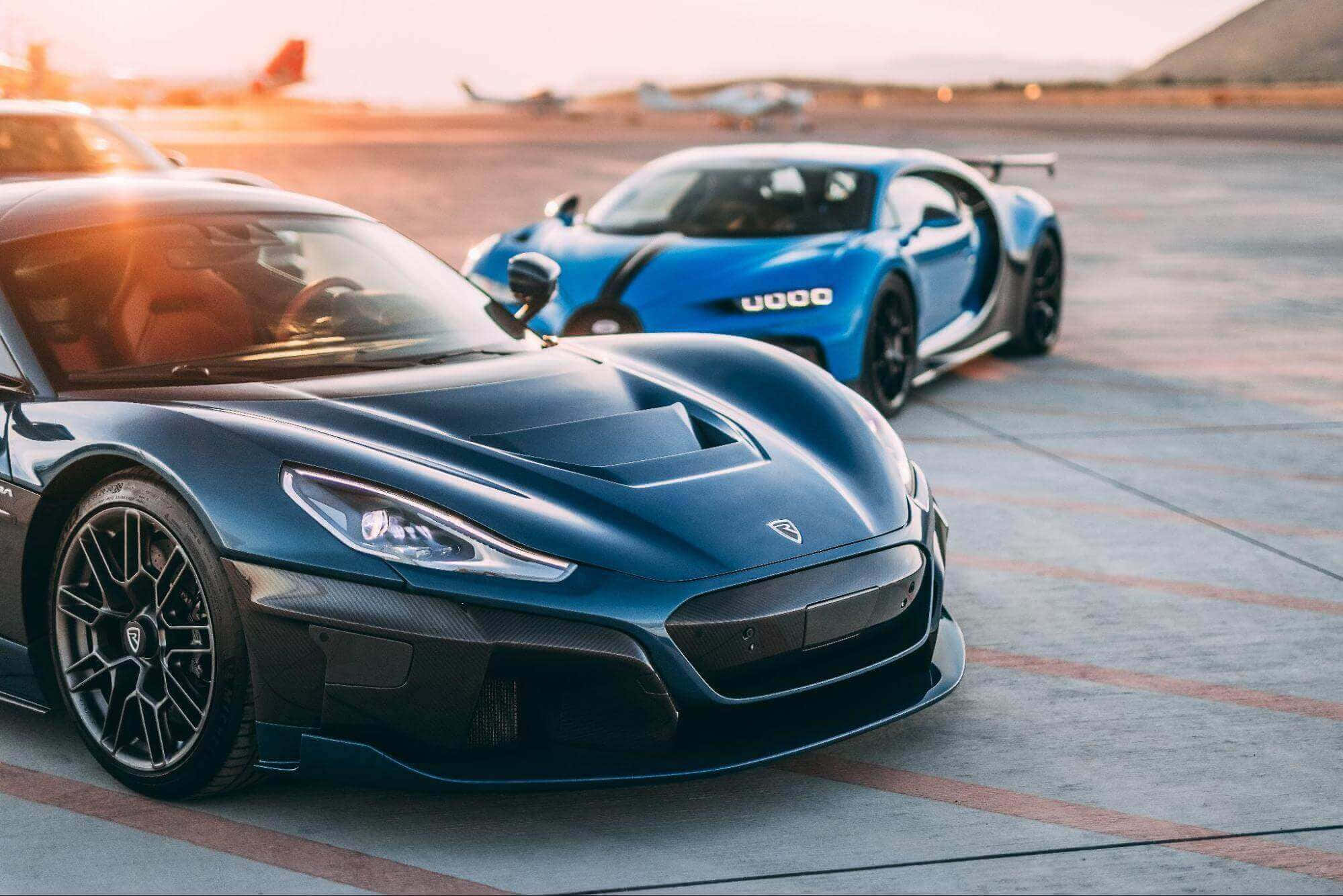 流線型Rimac電動超跑行駛中 壁紙 — 兩輛時尚超跑，一輛深藍色和一輛亮藍色，停在沐浴在金色夕陽下的機場停機坪上。