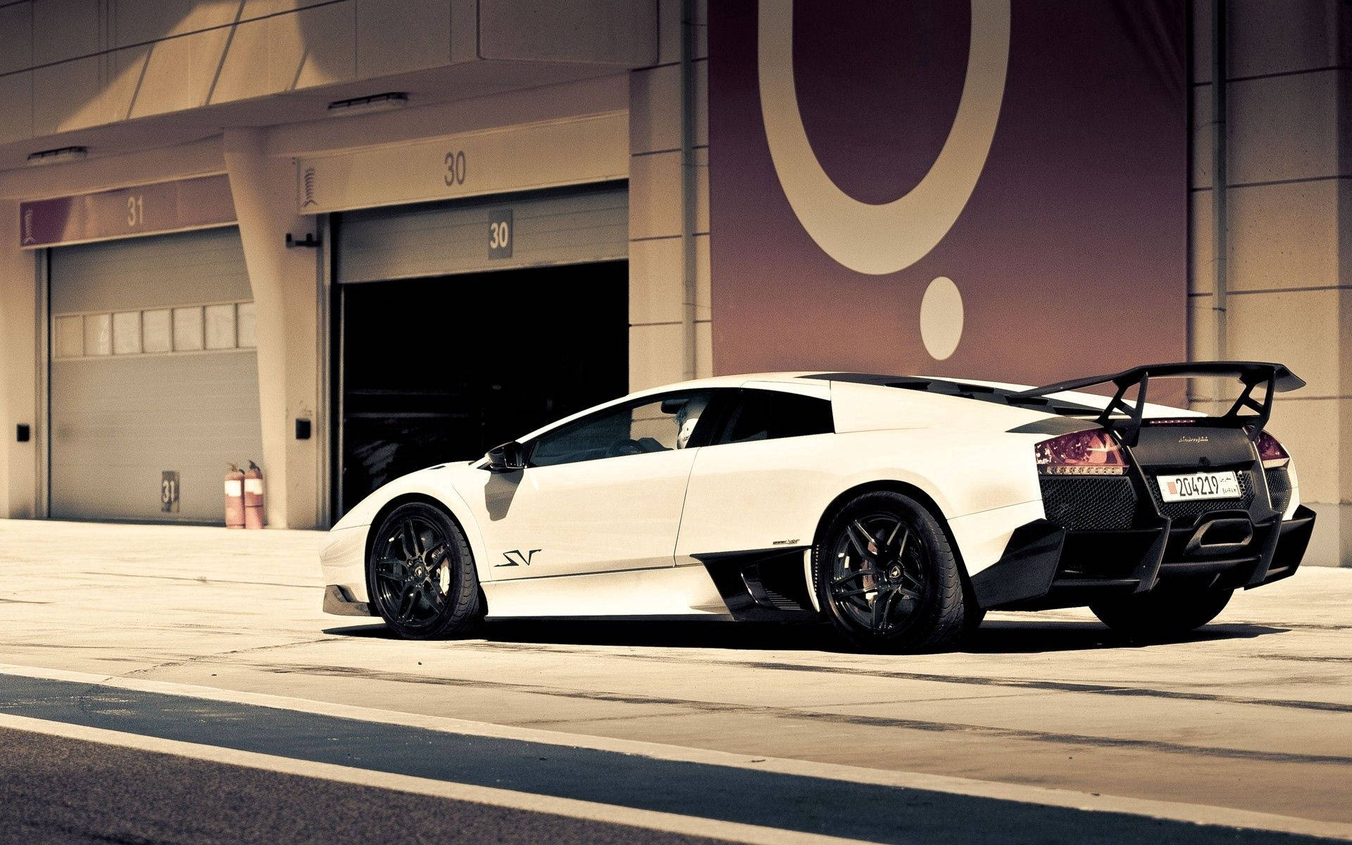 日落時分，白色林寶堅尼 Murciélago 停泊在工業車庫門前。