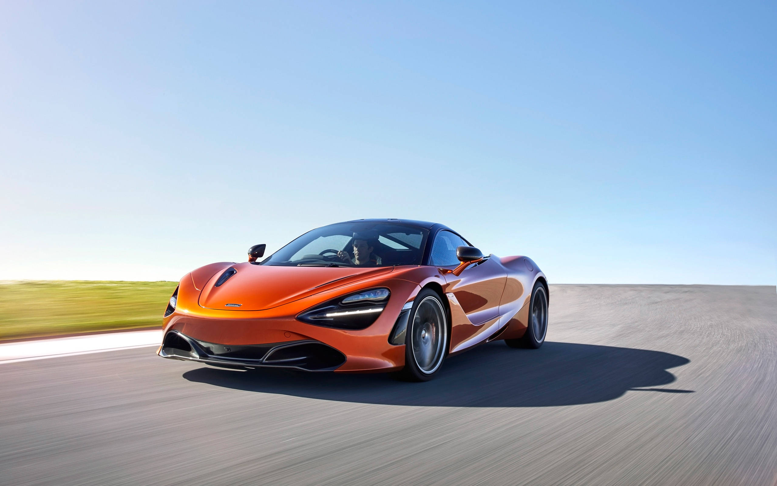 流線型橙色麥拉倫720s 4K 壁紙 — 一輛鮮豔的橙色McLaren 720S在晴朗藍天下沿著陽光明媚的沙漠公路飛馳。